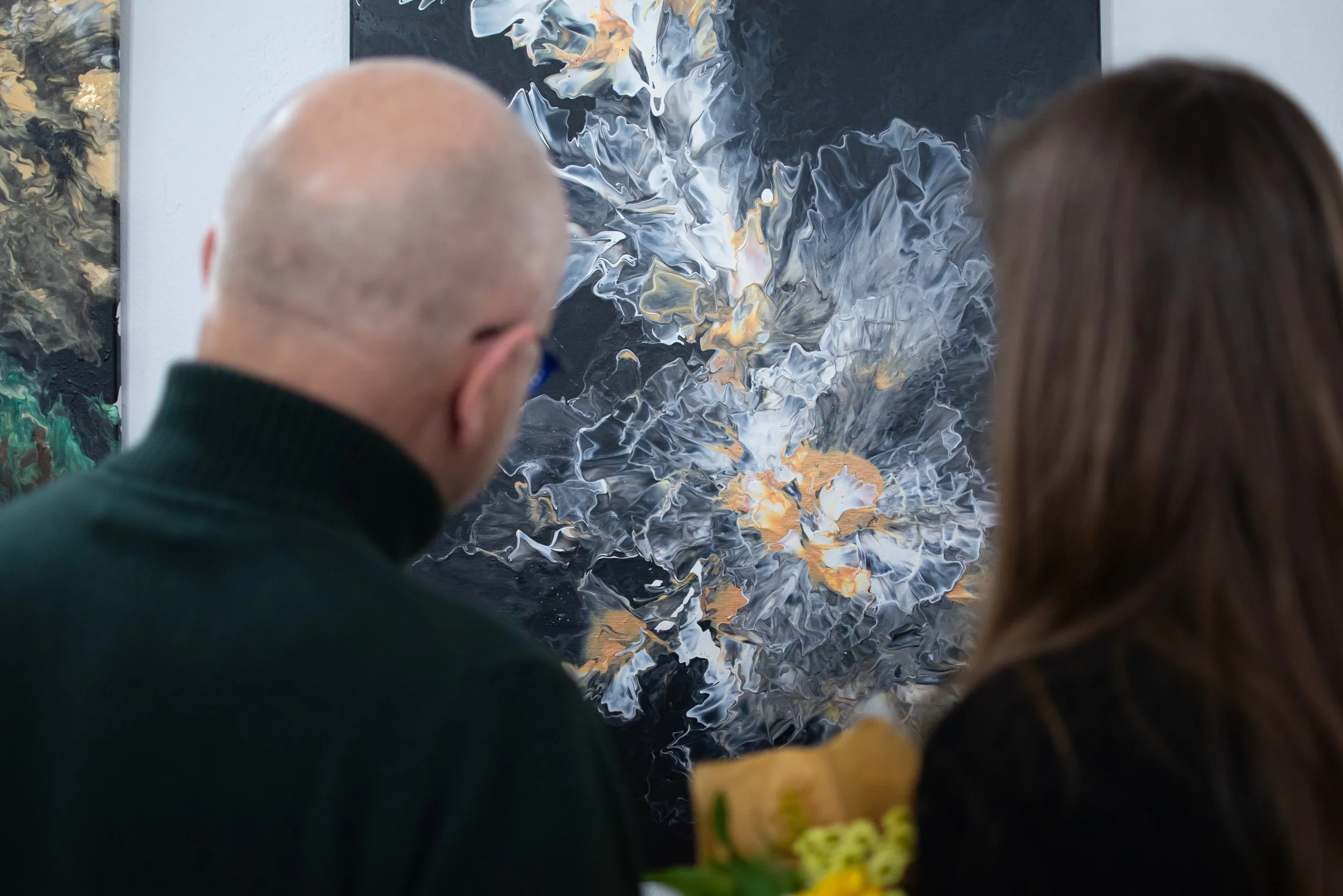 Two people viewing abstract artwork with black, white, gray, and hints of earthy tones at an art gallery.