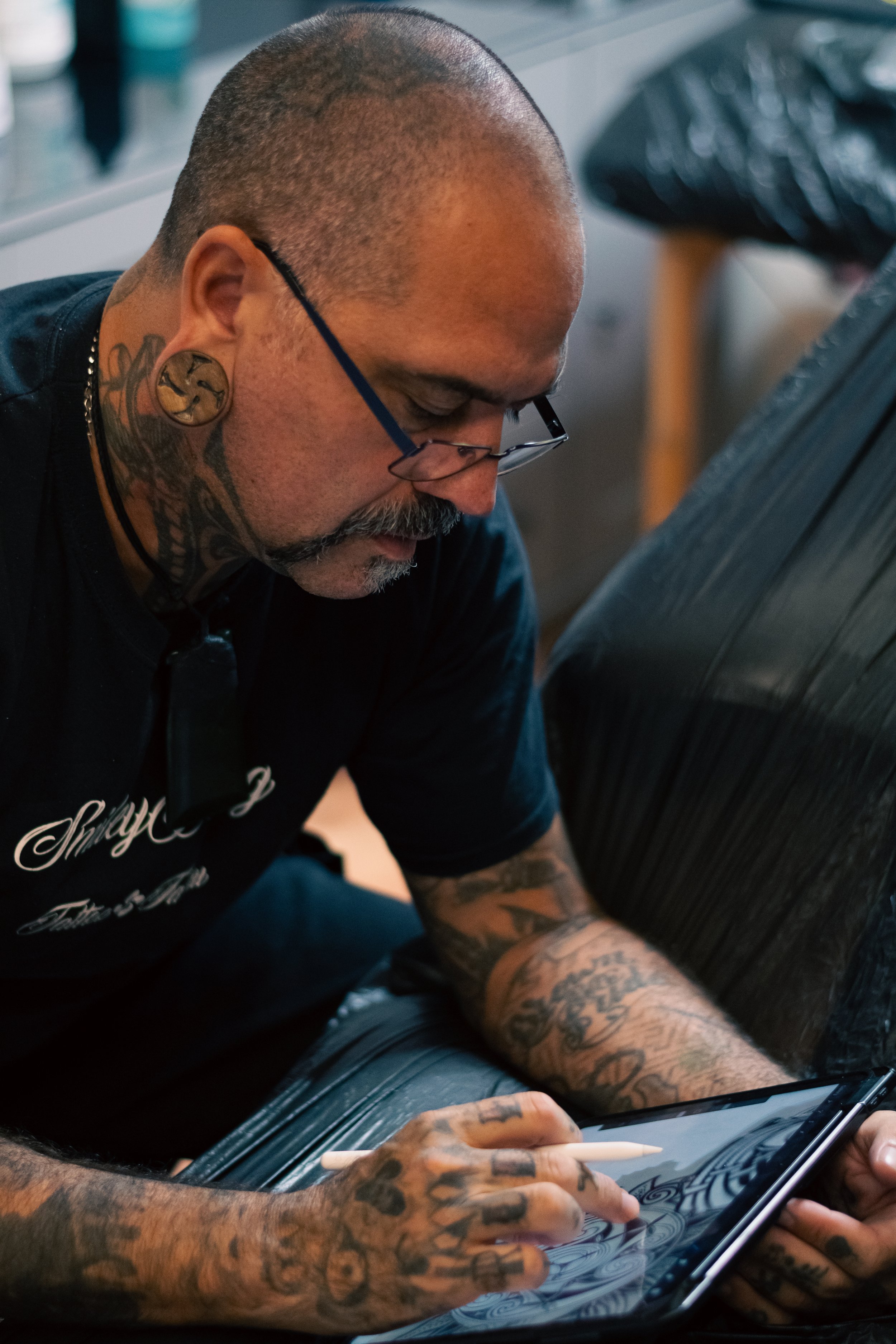 Tattooed man wearing glasses working on a digital tablet with stylus