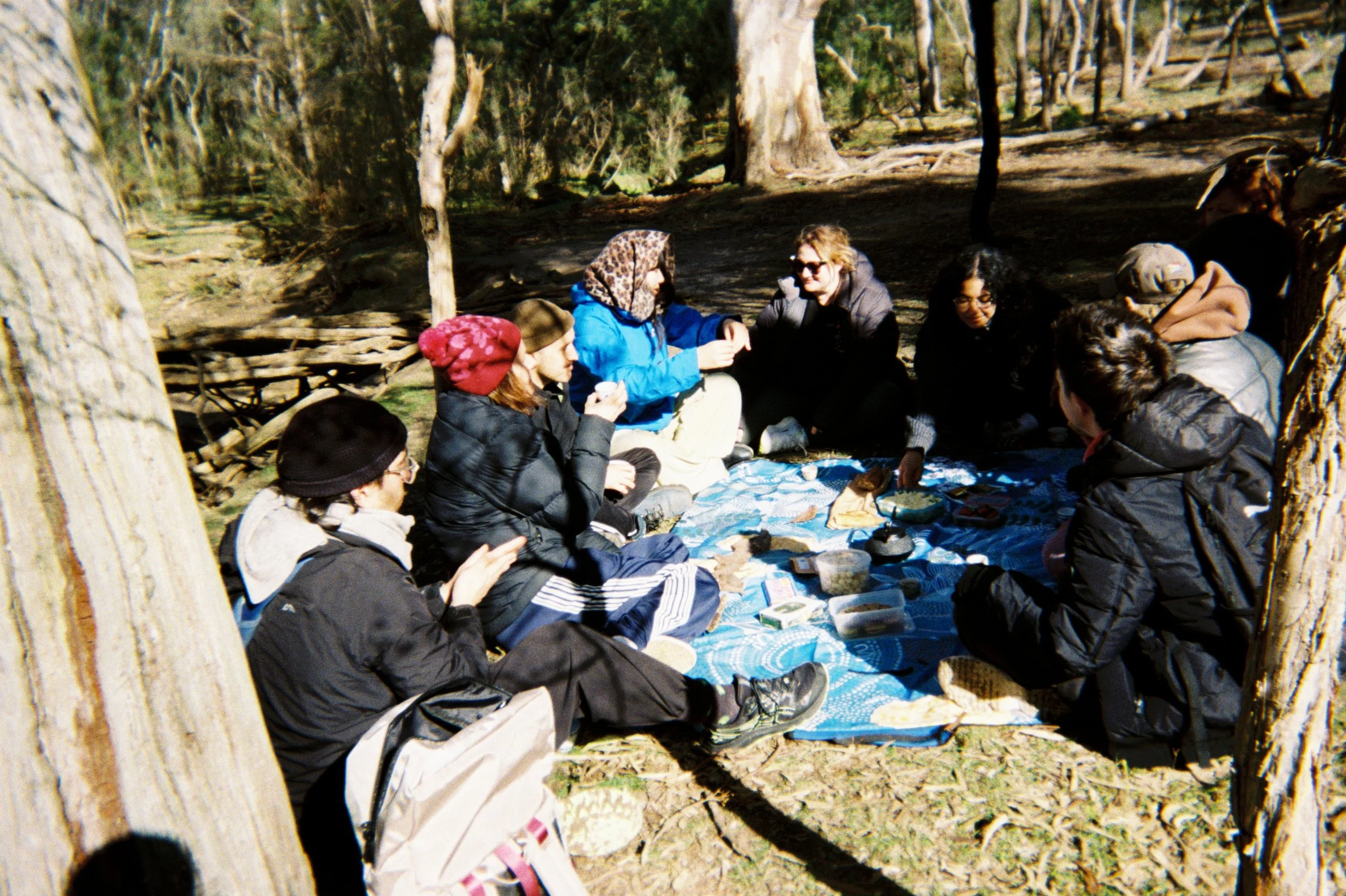Group of 10 people sitting down outside on a picnic rug