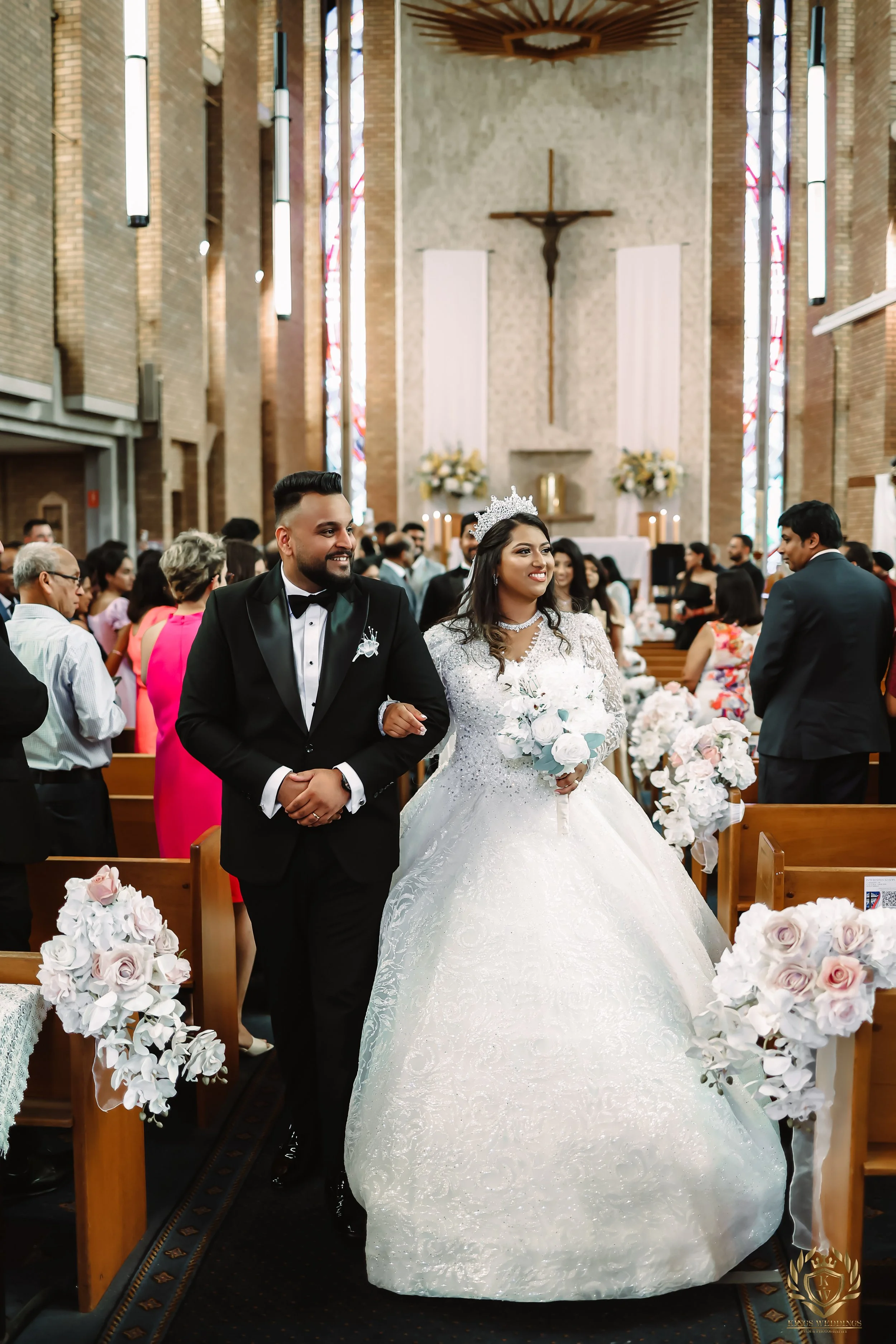 A bride and groom walking down the aisle inside a church with guests.Capture your Liverpool wedding with cinematic film and photography. KingsWeddings creates timeless memories of your special day.