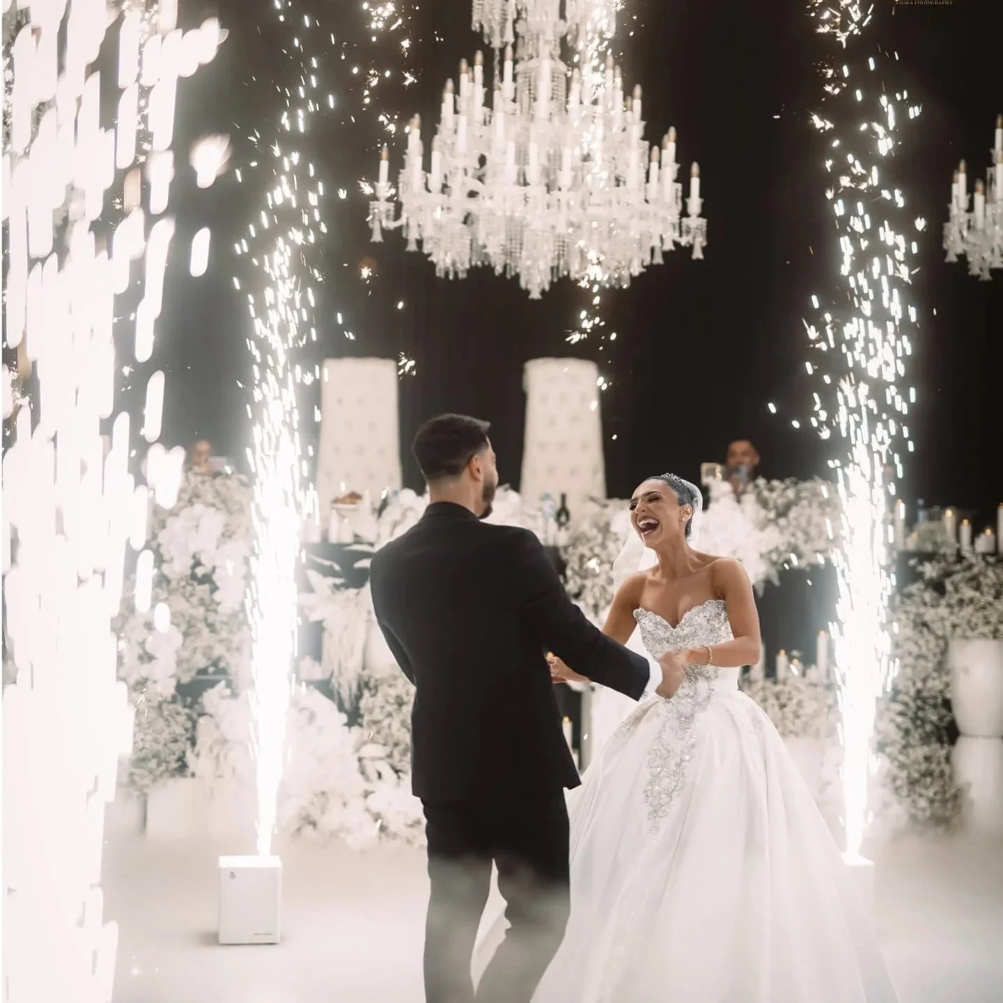 A bride and groom dancing at their wedding reception surrounded by sparklers and chandeliers.