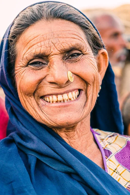 Elderly Pakistani woman smiling, wearing a blue headscarf and patterned shirt
