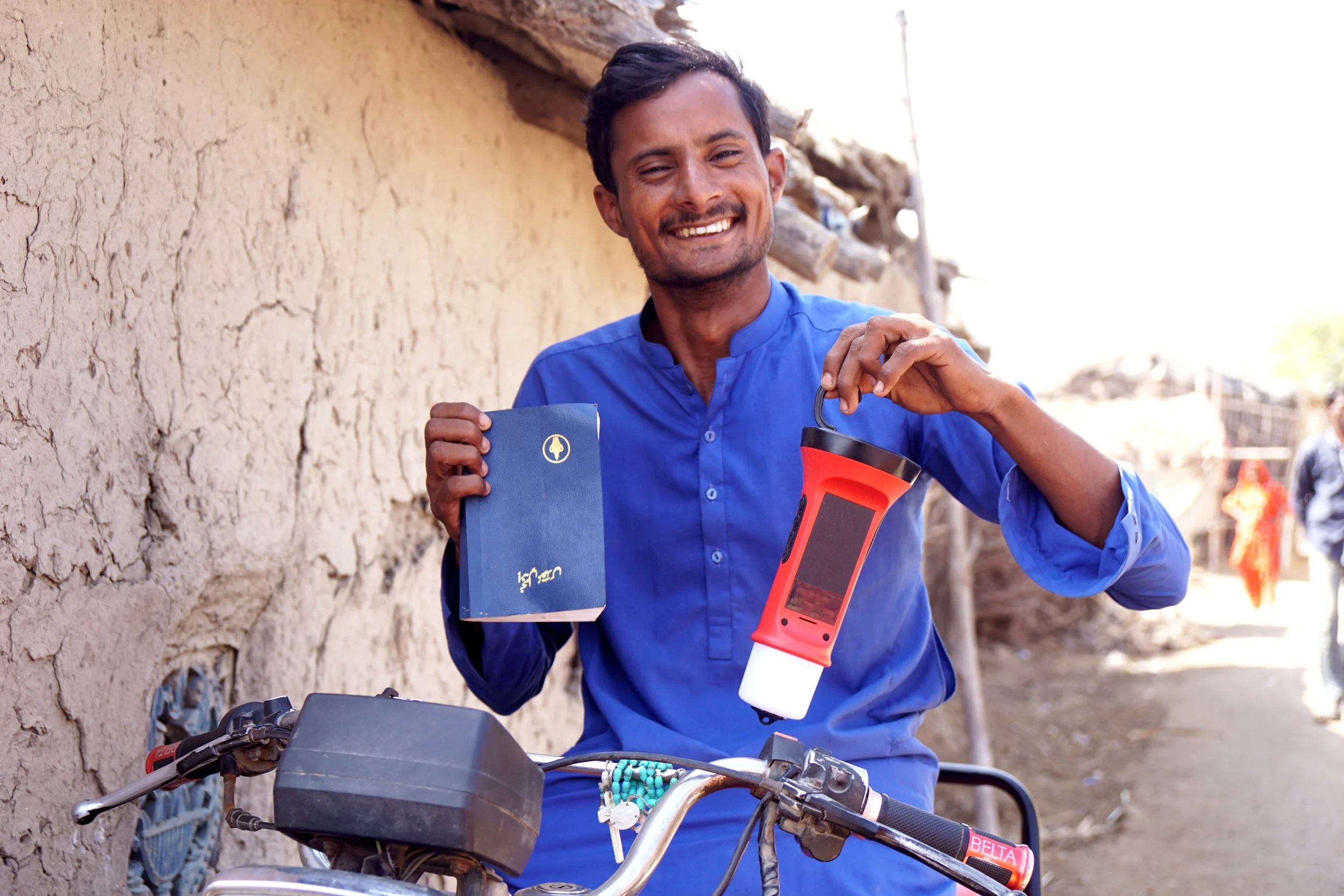 Pakistani man smiling with bible and torch on motorbike in rural village in Pakistan.