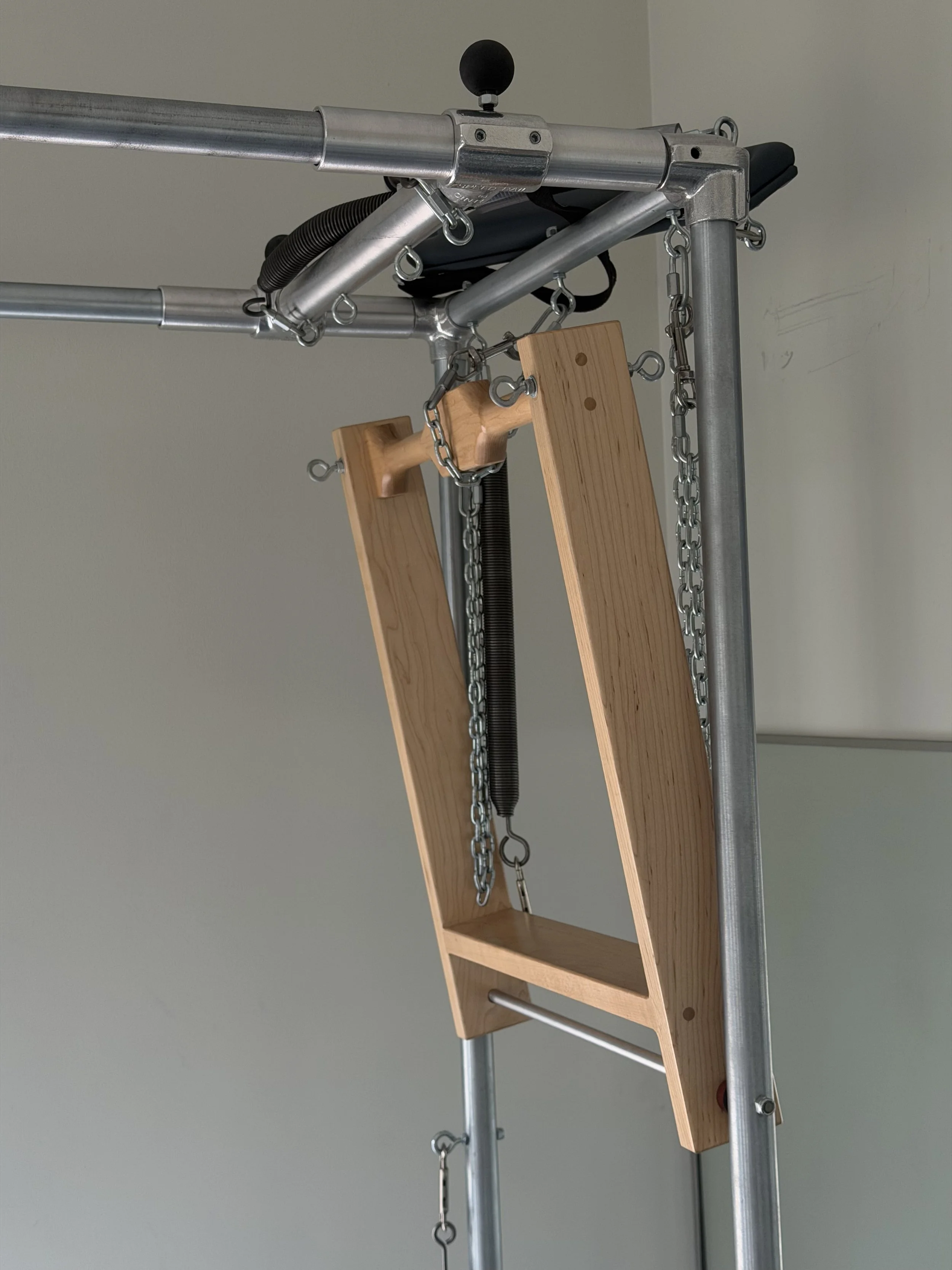 A Pilates Cadillac machine with a wooden platform and metal chains for exercising.