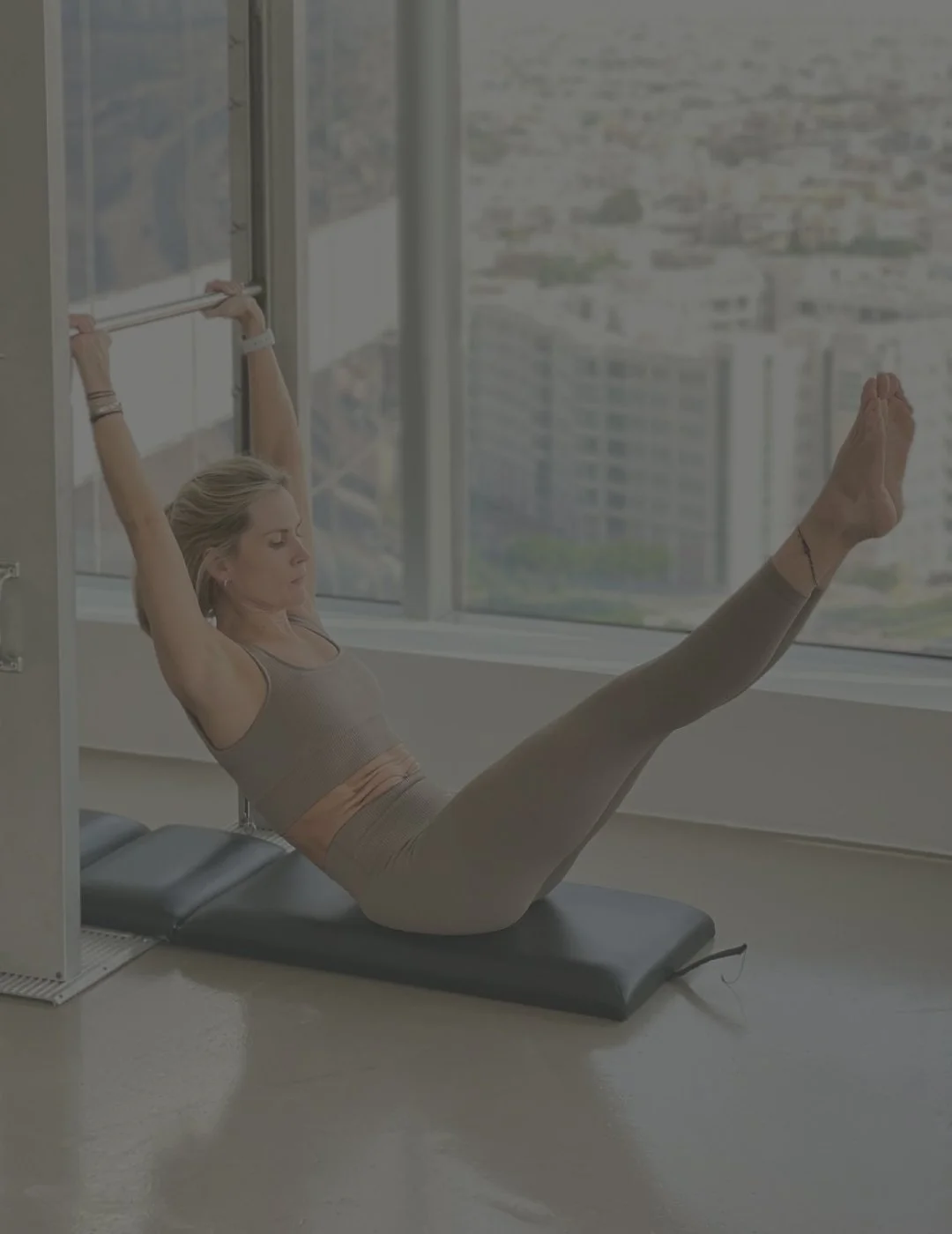 Woman exercising on yoga mat near large window with cityscape view.