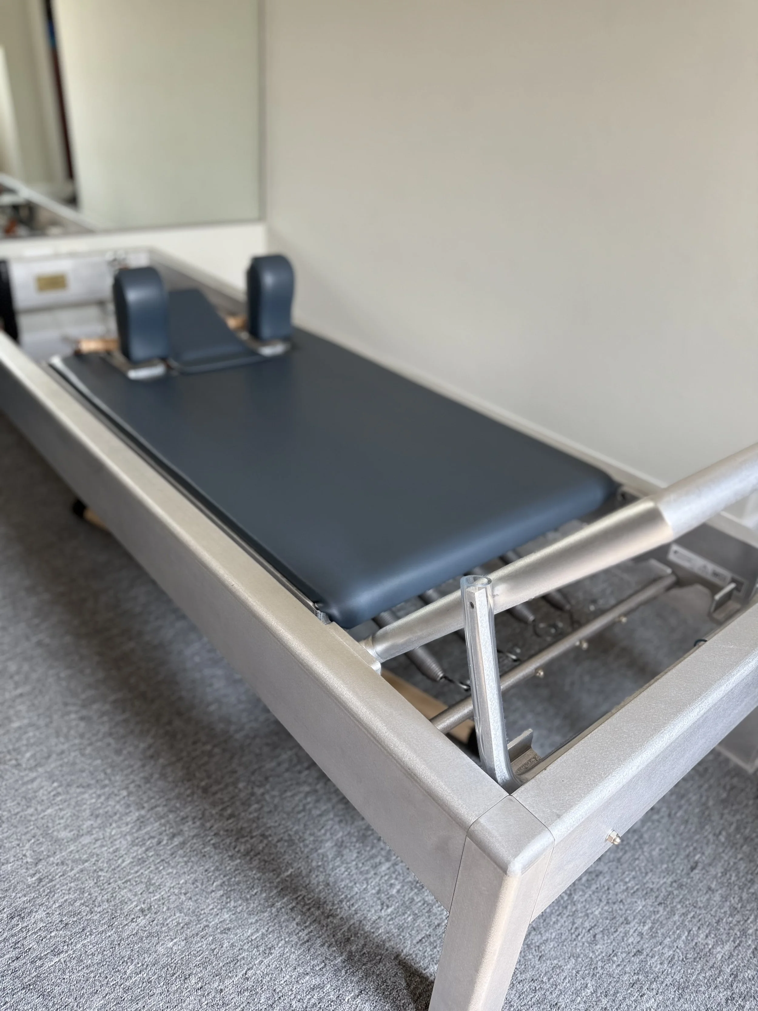 Hospital stretcher with black padding, side rails, and head supports in a room with gray carpet and white walls.