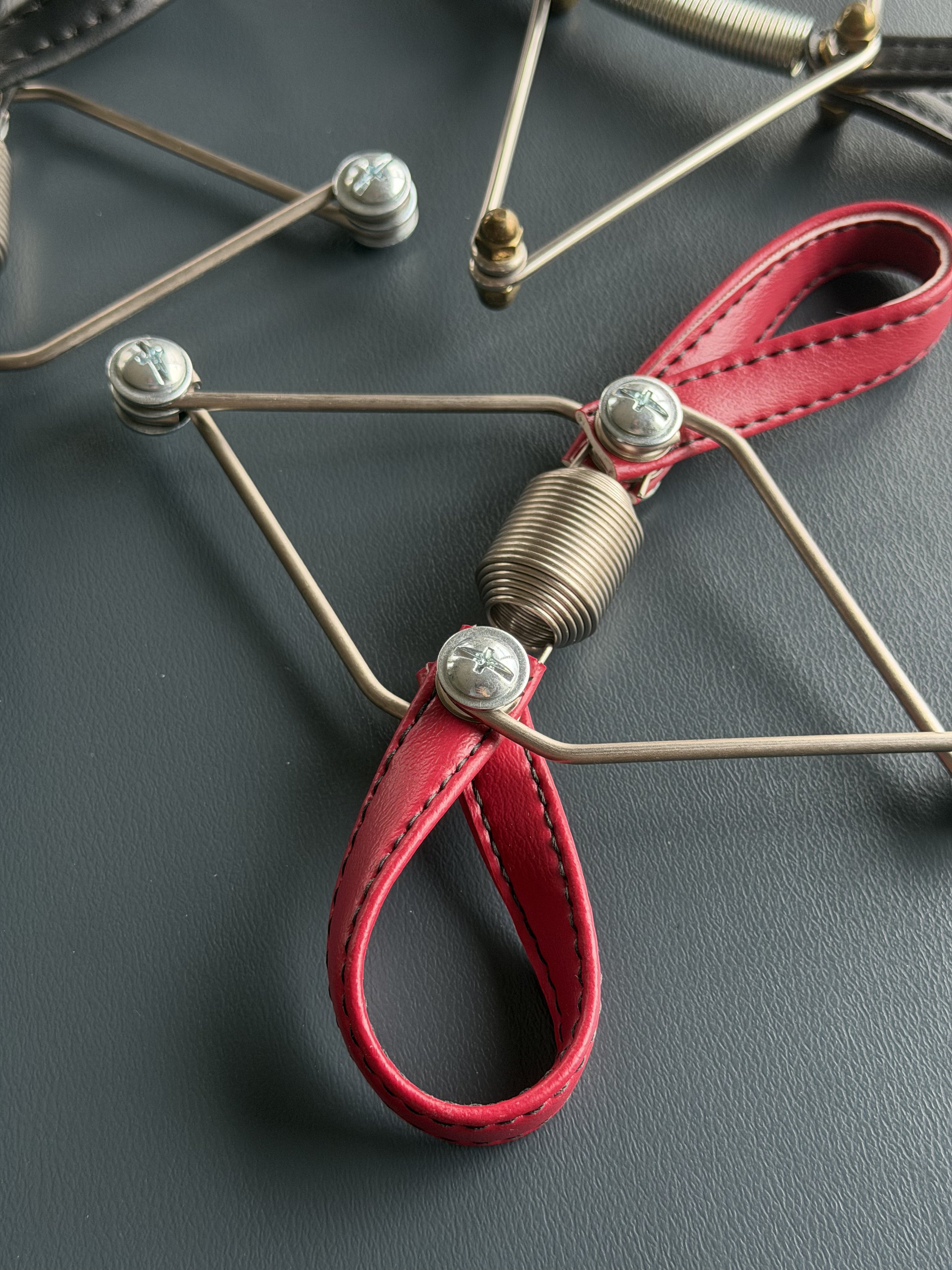Close-up of a metal head massager with a red leather strap, resting on a black surface.