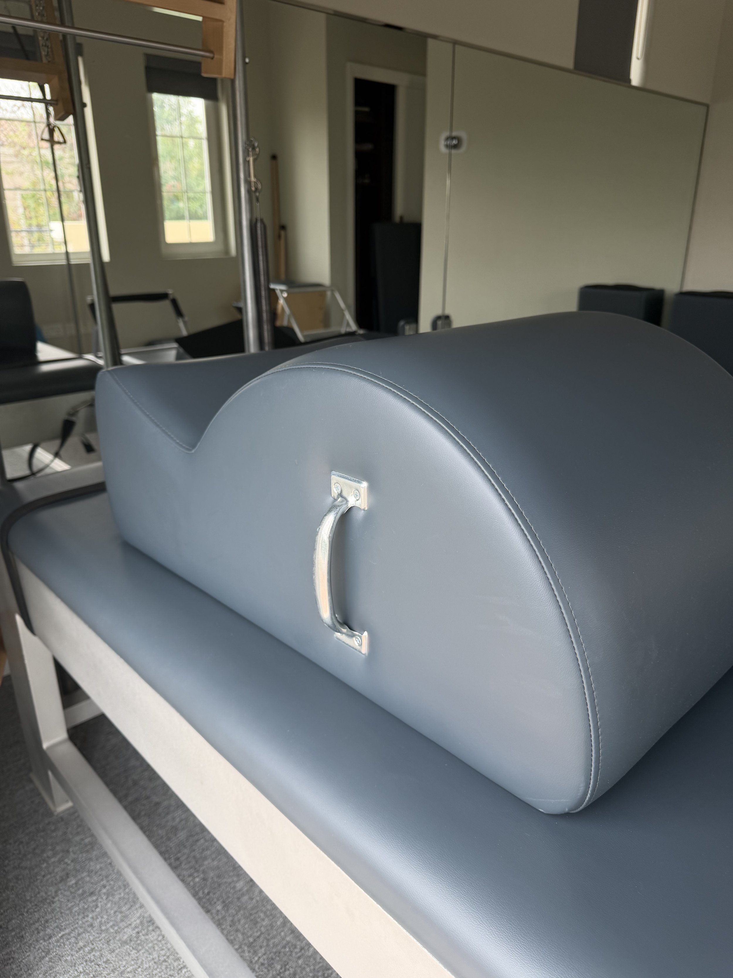 Medical examination table with a blue padded headrest and a metal handle in a room with windows and mirrors.