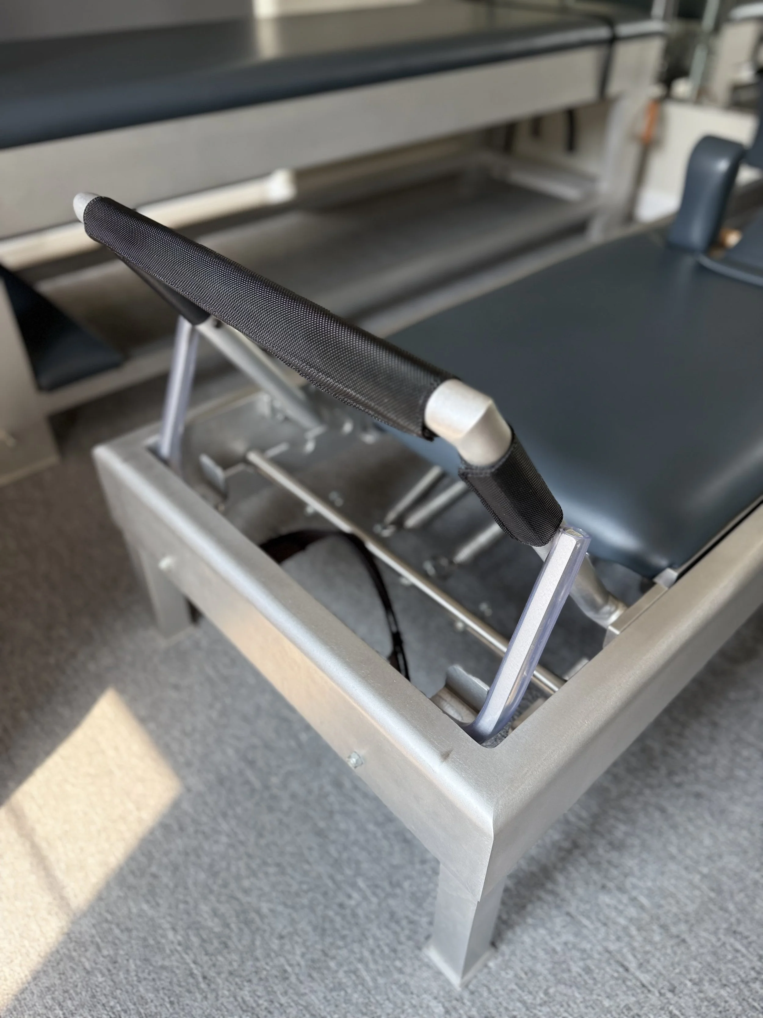 Close-up of a hospital or medical stretcher with an adjustable handle, made of metal and black mesh material, in a clinical setting.