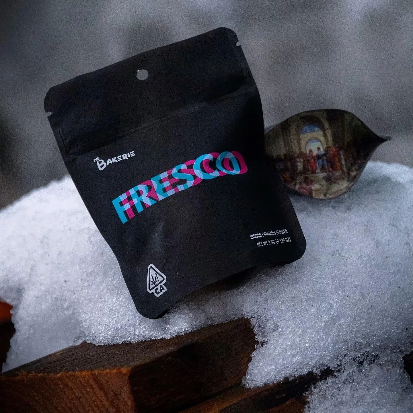 Black package of Fierressa indoor cannabis flower on snow with a reflective ornament nearby.  - designed by Peter Sobat