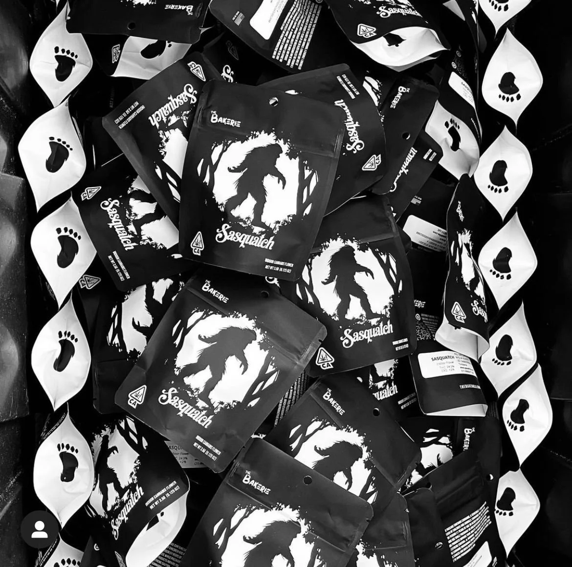 A pile of Sasquatch-themed cannabis packaging with a silhouette of a Bigfoot creature in a forest scene.