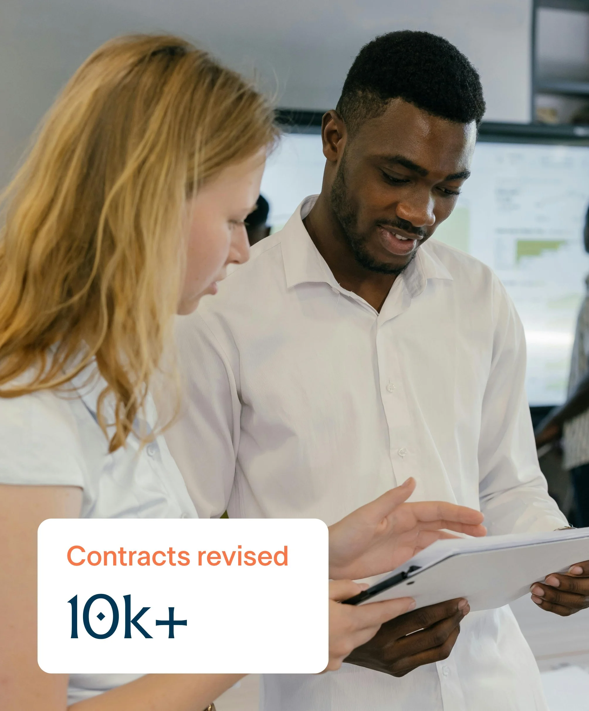 Two professionals in a business meeting looking at a tablet in their hands with the words 10k+ contracts revised.