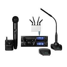 Wireless microphone, wireless router with four antennas, digital audio mixer, desk lamp, and a small black device.