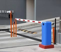 A parking barrier gate with an orange arm, blue and white base, and black and yellow striped safety stop, in a parking lot.