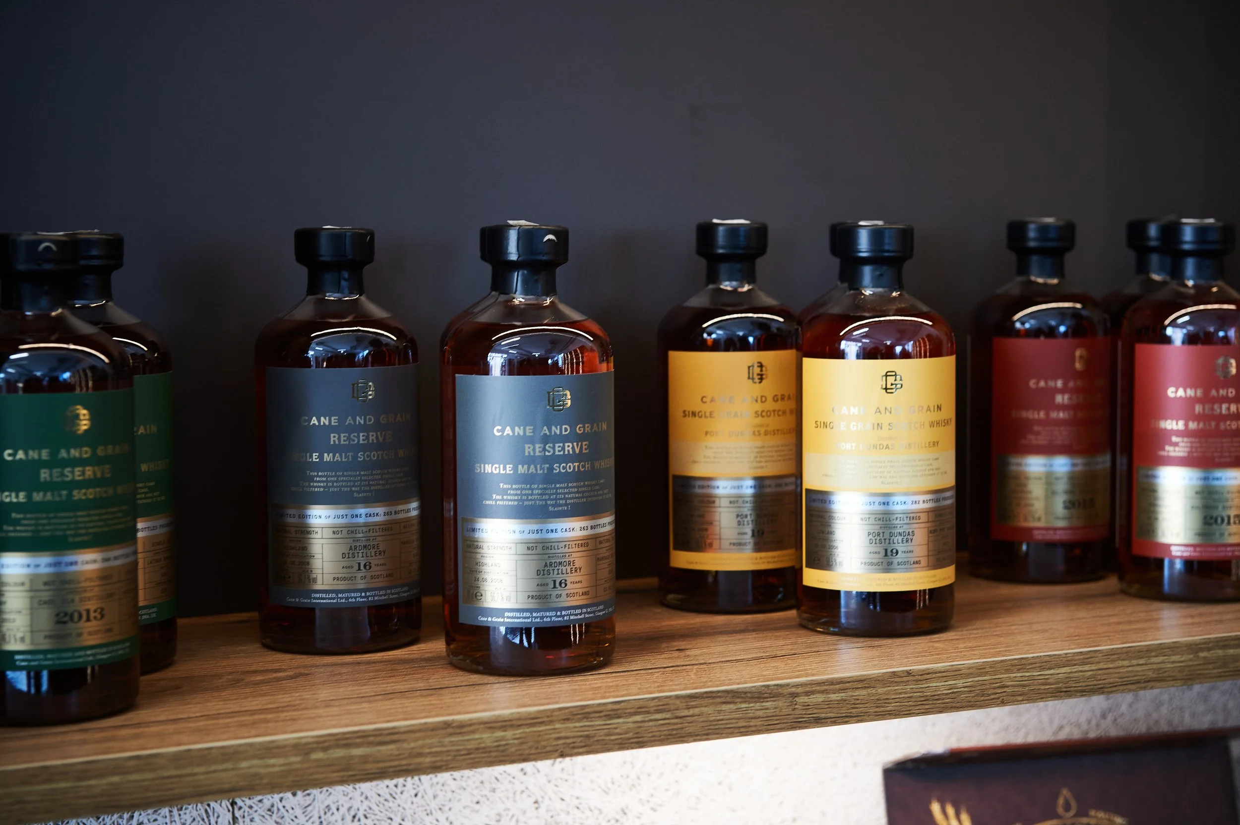 Brennereiflaschen auf einem Holzregal, etikettiert mit verschiedenen Jahrgängen und Editionen, einschließlich Whisky.