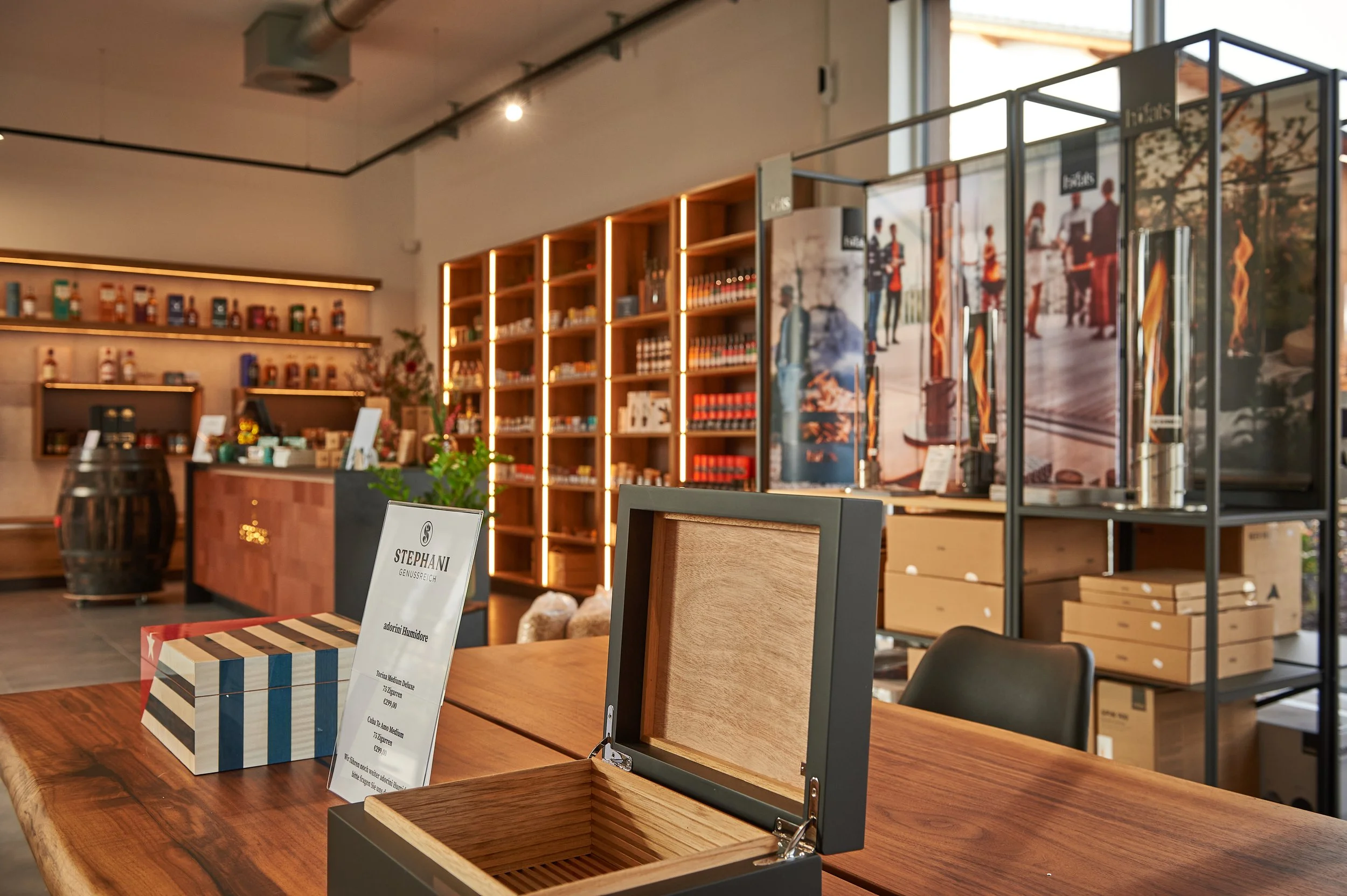 Innenansicht eines stores mit Holzregalen, die mit Produkten gefüllt sind, einem Verkaufstresen im Hintergrund, und einer Tafel mit Text. Im Vordergrund liegen offene und geschlossene Holzboxen auf einem Holztablett.