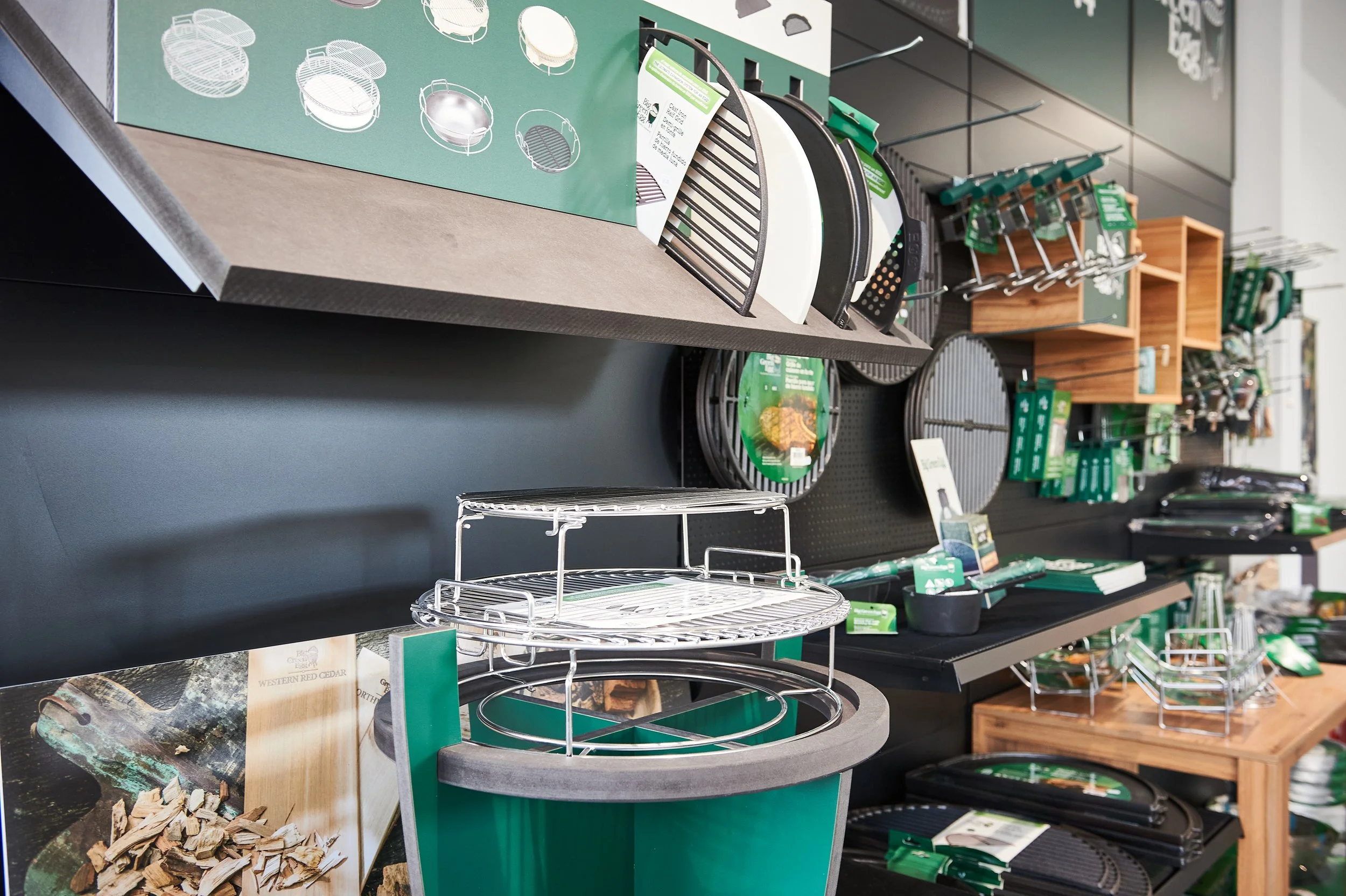 Verschiedene Grill- und Barbecuezubehörteile, wie Grillroste, Grillkörbe und Zubehör für den Außenbereich, in einem Geschäft ausgestellt.