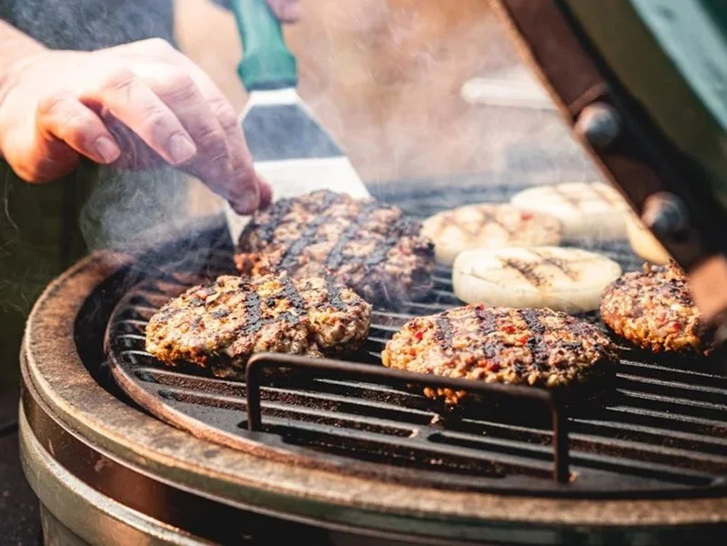Grill mit Hamburger-Patties, Zwiebelringen und einem Fleischstück, das gegrillt wird.