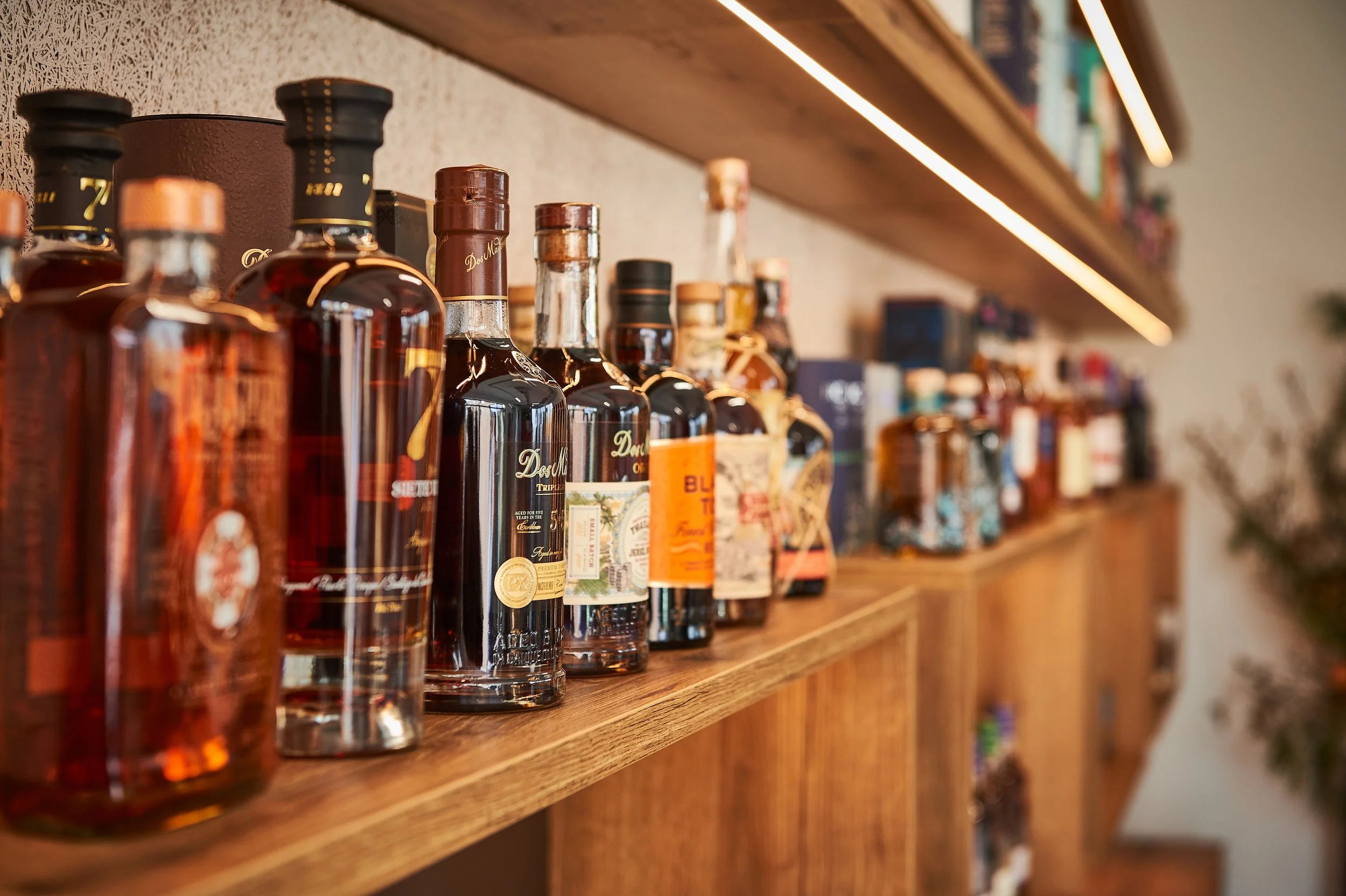 Brennweiteaufnahme von einer Holzregal mit verschiedenen alkoholischen Spirituosenflaschen, hauptsächlich Whiskey, in einer Bar oder einem Verkaufsraum, unscharfer Hintergrund.