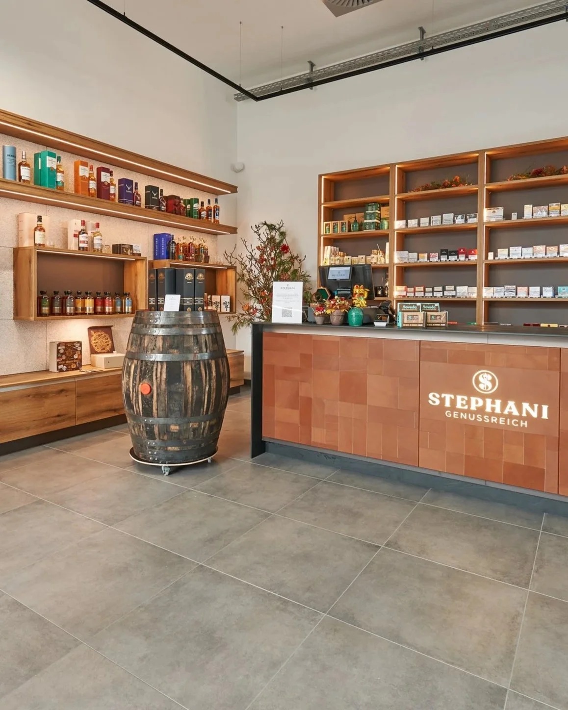 Inneneinrichtung eines Fachgeschäfts namens Stephani Genussreich mit Warenregalen, einem Tresen und einem Weinfass.