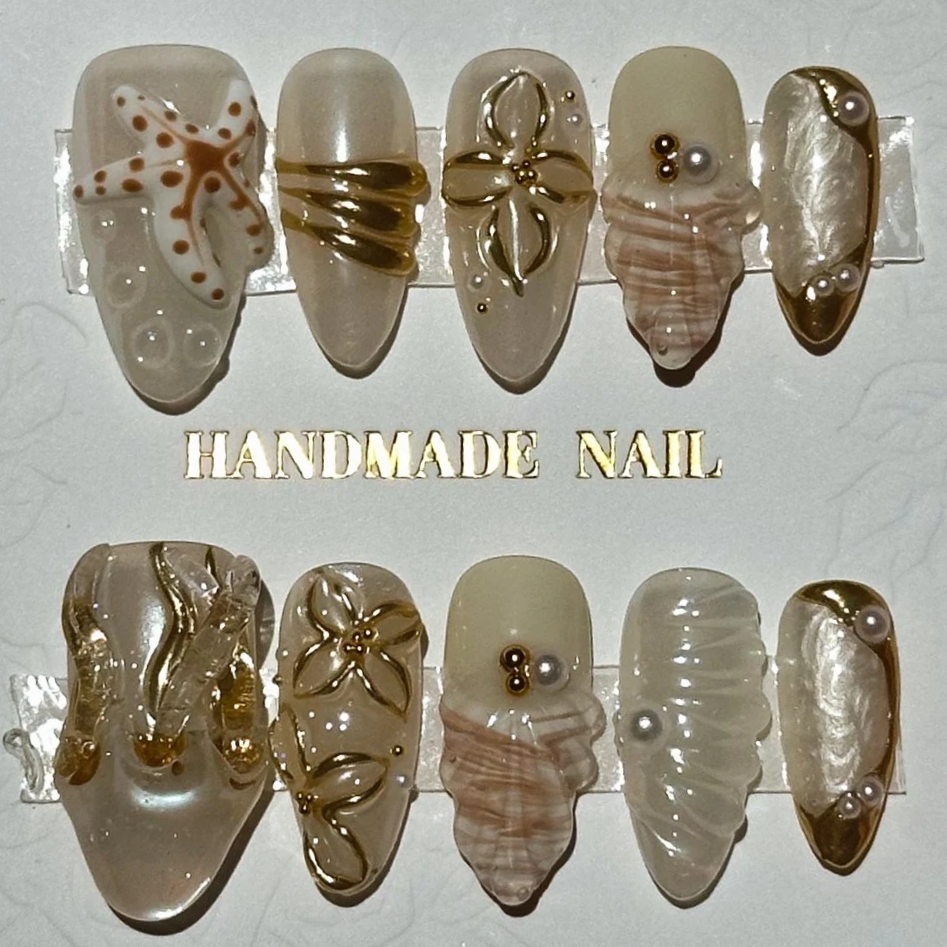 Set of 10 handmade press on nails with decorative designs, some featuring gold accents, pearls, and floral patterns. 