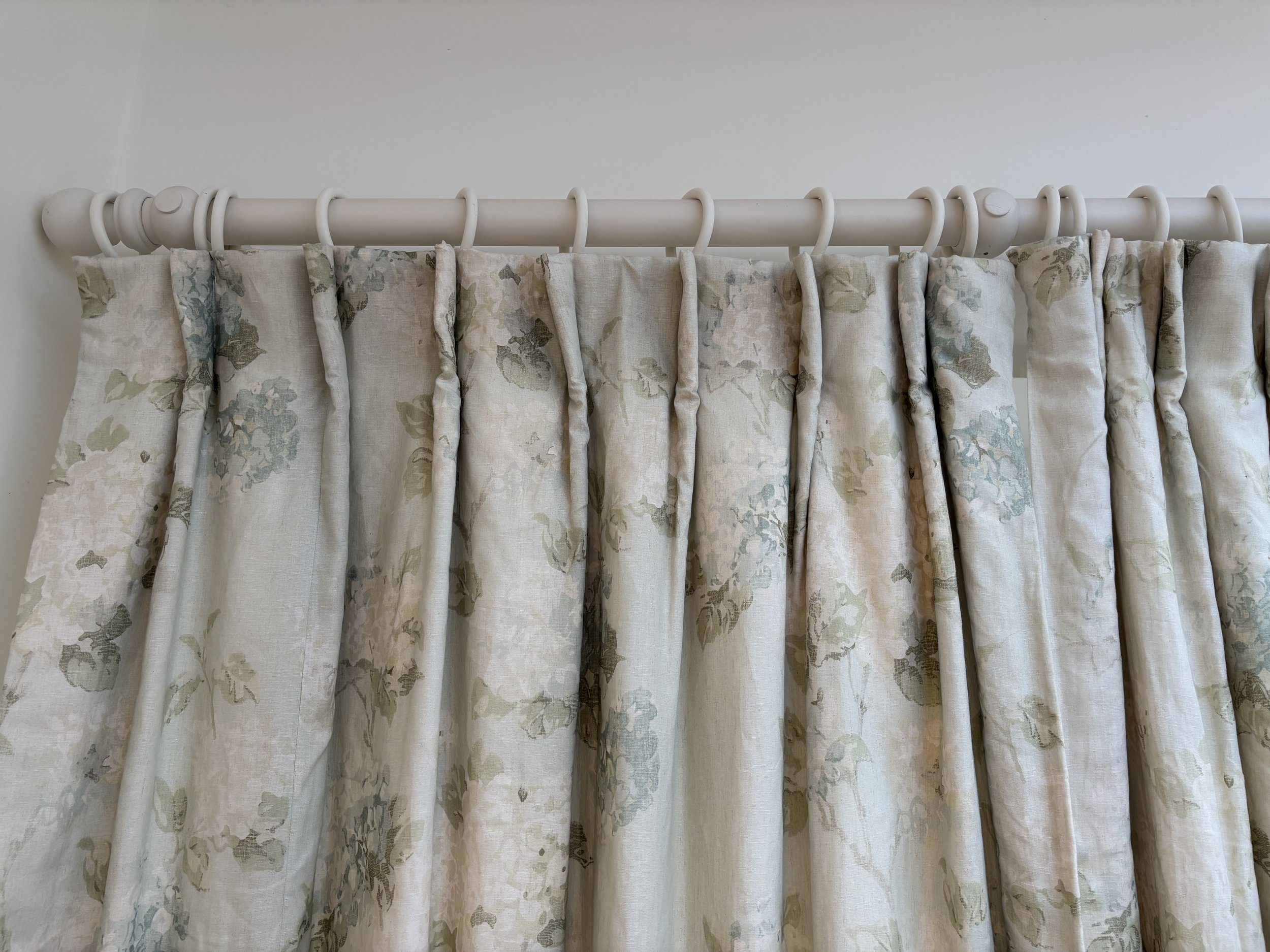 Cream-colored floral curtains hanging from a white curtain pole.
