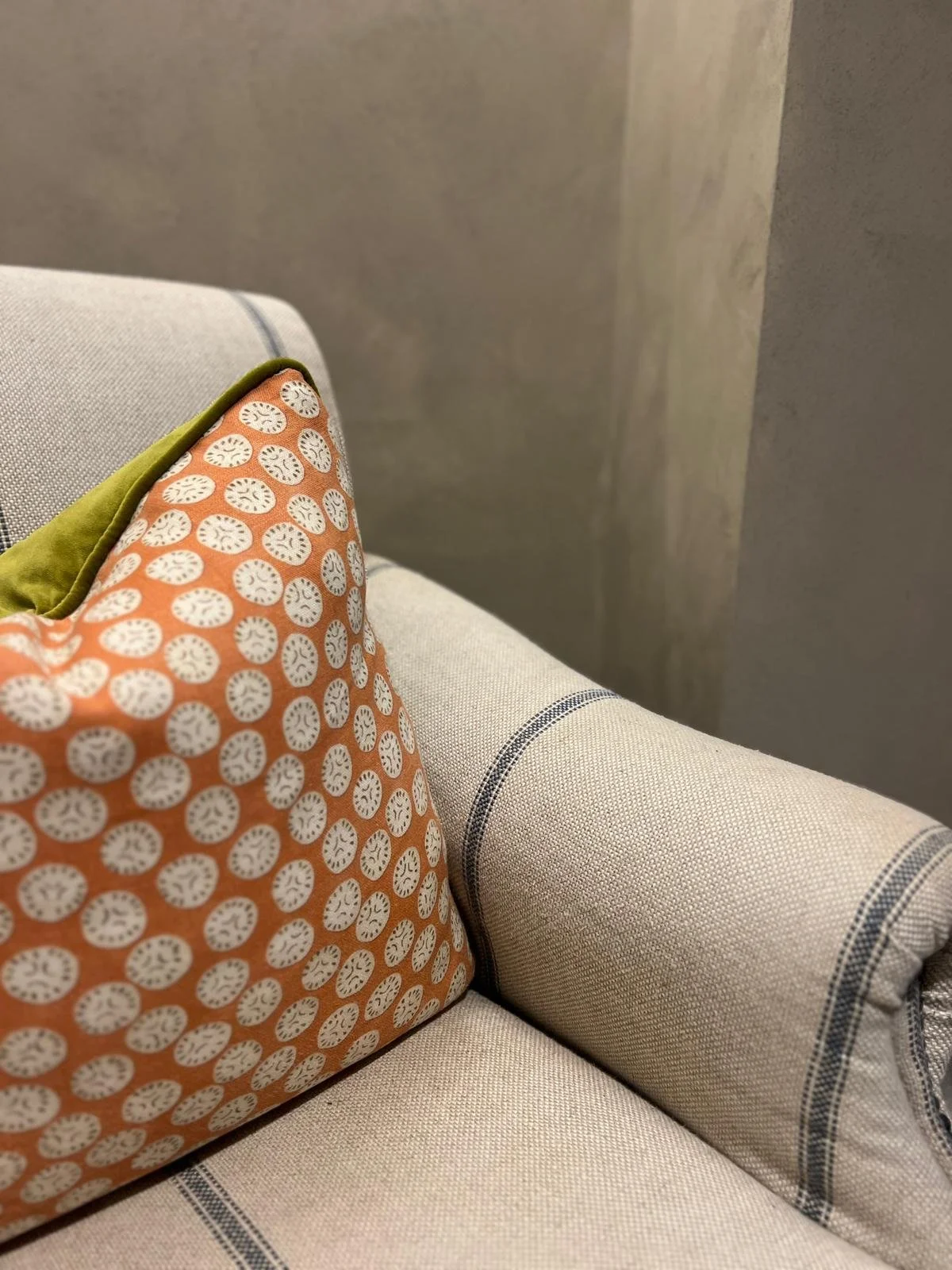 Close-up of a sofa with striped linen fabric pattern, decorated with an orange cushion with white circular patterns and a green pillow.