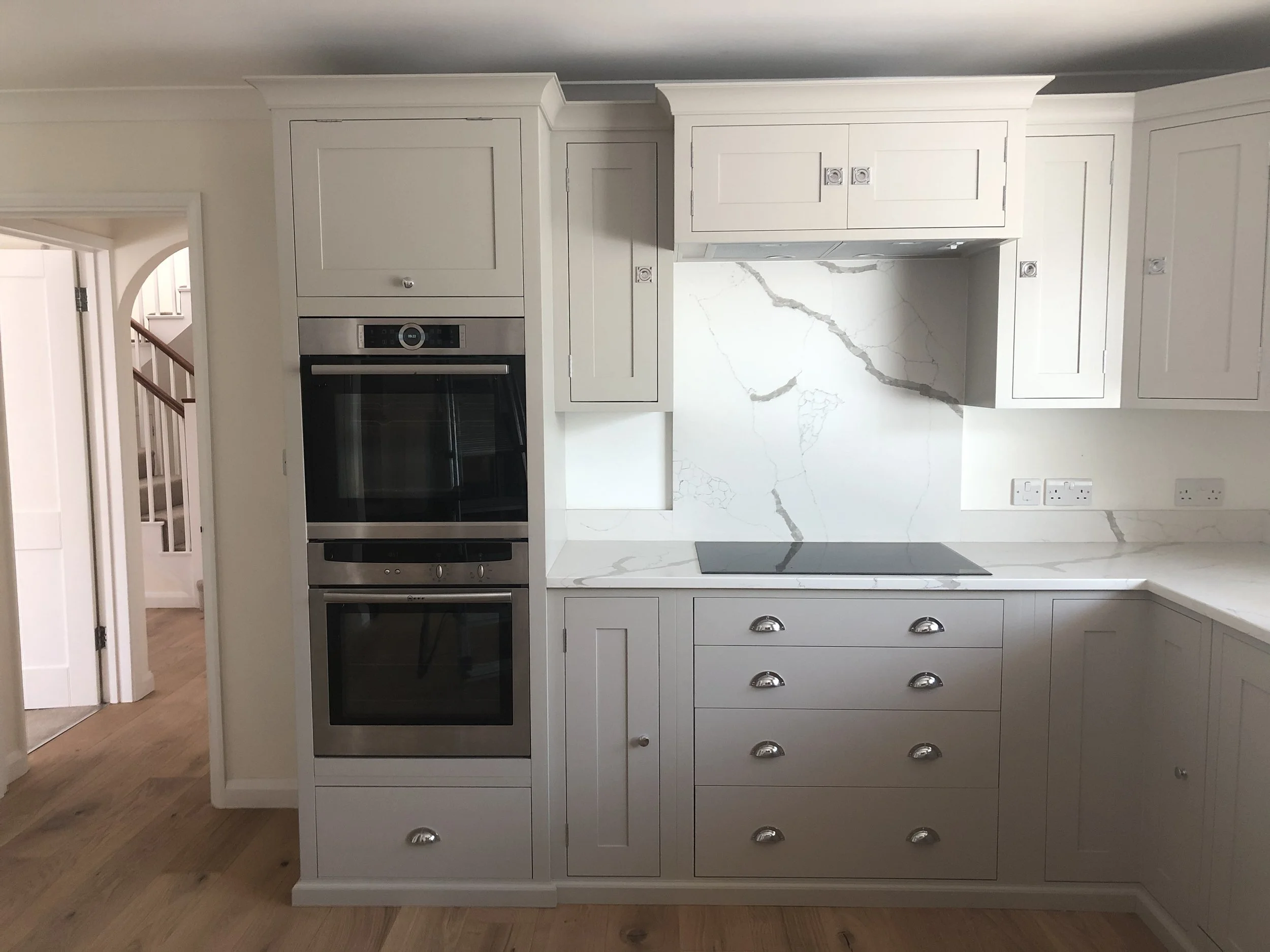Modern kitchen with white cabinetry, marble countertops, and a built-in double oven.
