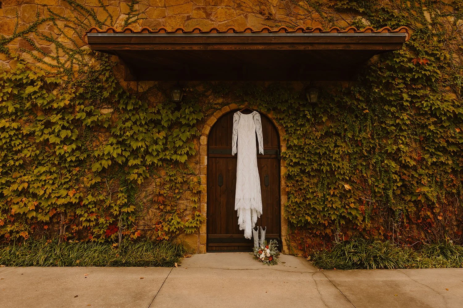 Wedding dress hanging outside a lush green wall and rustic Tuscan wooden door