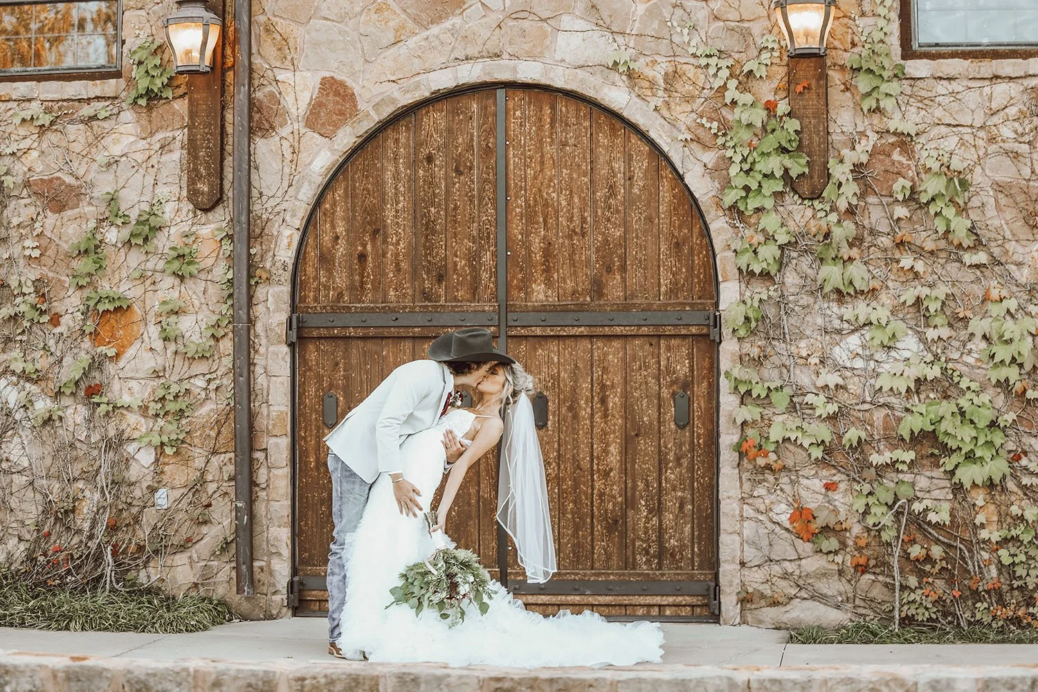 Wedding photo of a couple kissing in front of the Tuscan style building and rustic arched wooden door