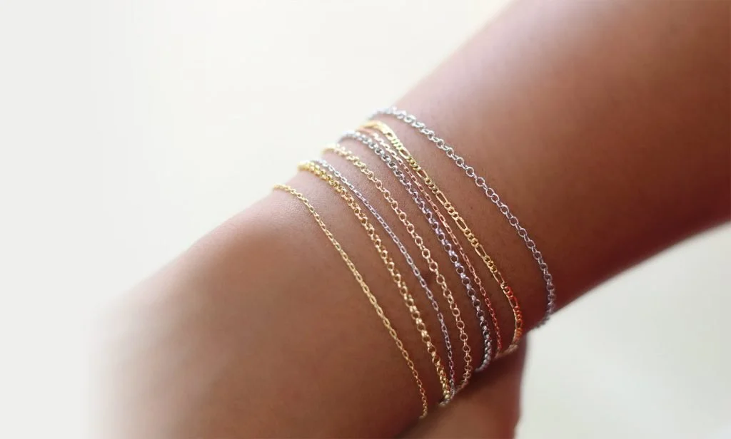 A wrist adorned with multiple delicate gold and silver chain bracelets.