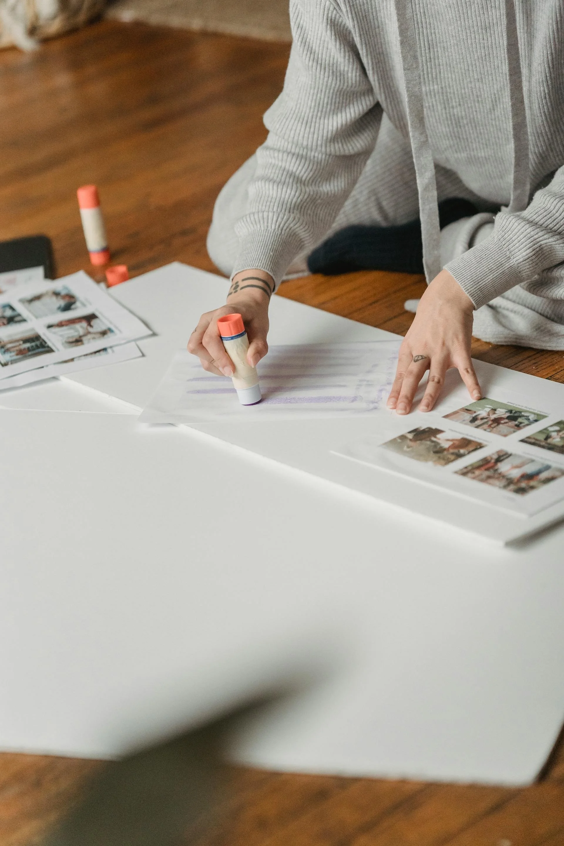 Persona che lavora su un progetto creativo, usando dei marker su delle stampe di fotografie e pagine con immagini. Sono appoggiate su una grande superficie bianca, probabilmente una scrivania o un tappetino da disegno.