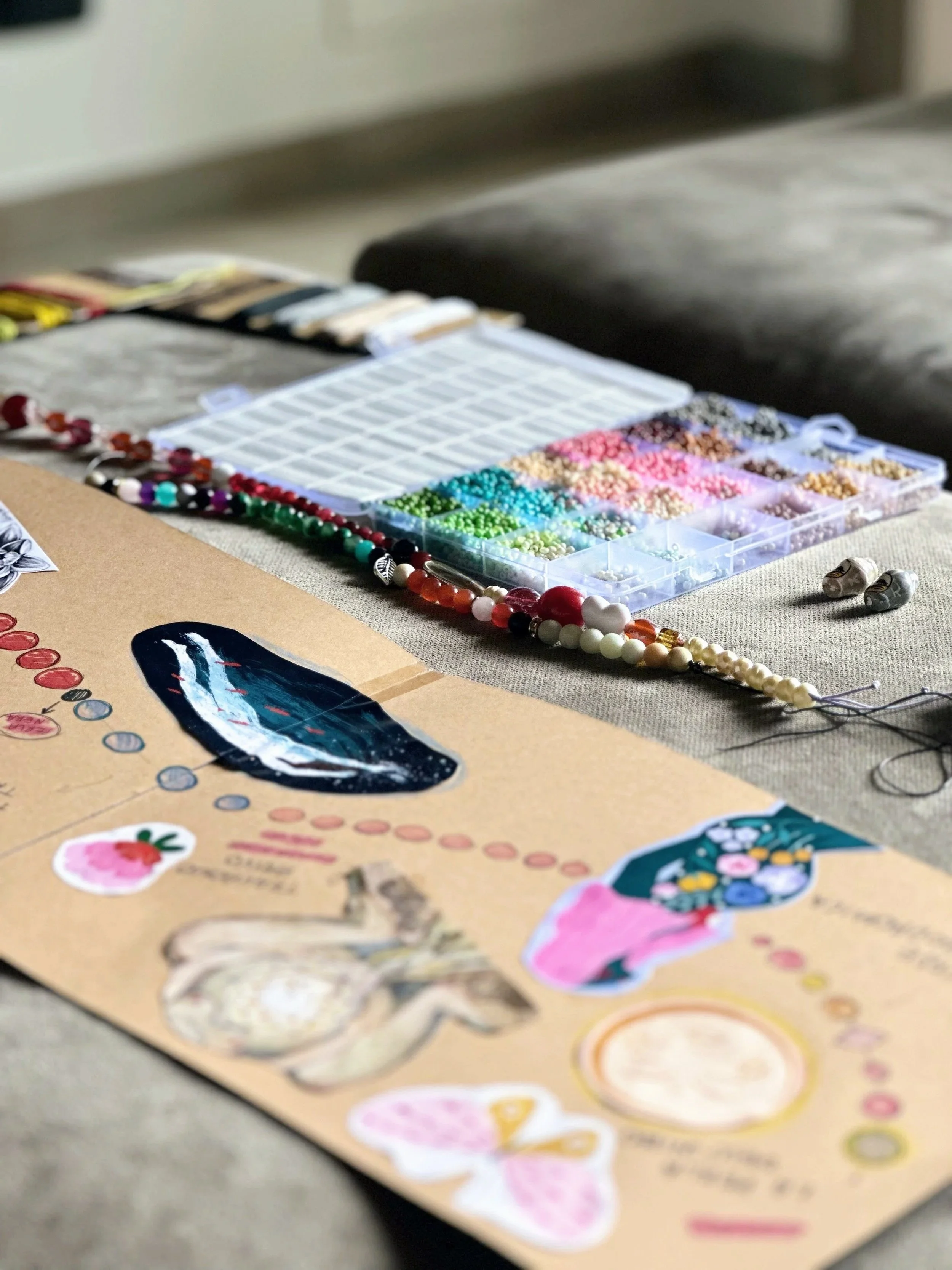 Materiali per creare gioielli, inclusi perline colorate, fili, e un esempio di progetto su un foglio di carta con disegni e annotazioni.