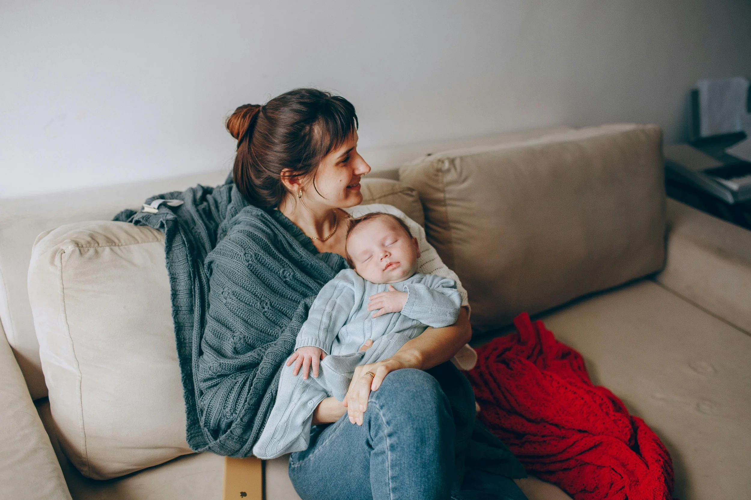 Una donna seduta su un divano, che tiene in braccio un bambino che dorme.