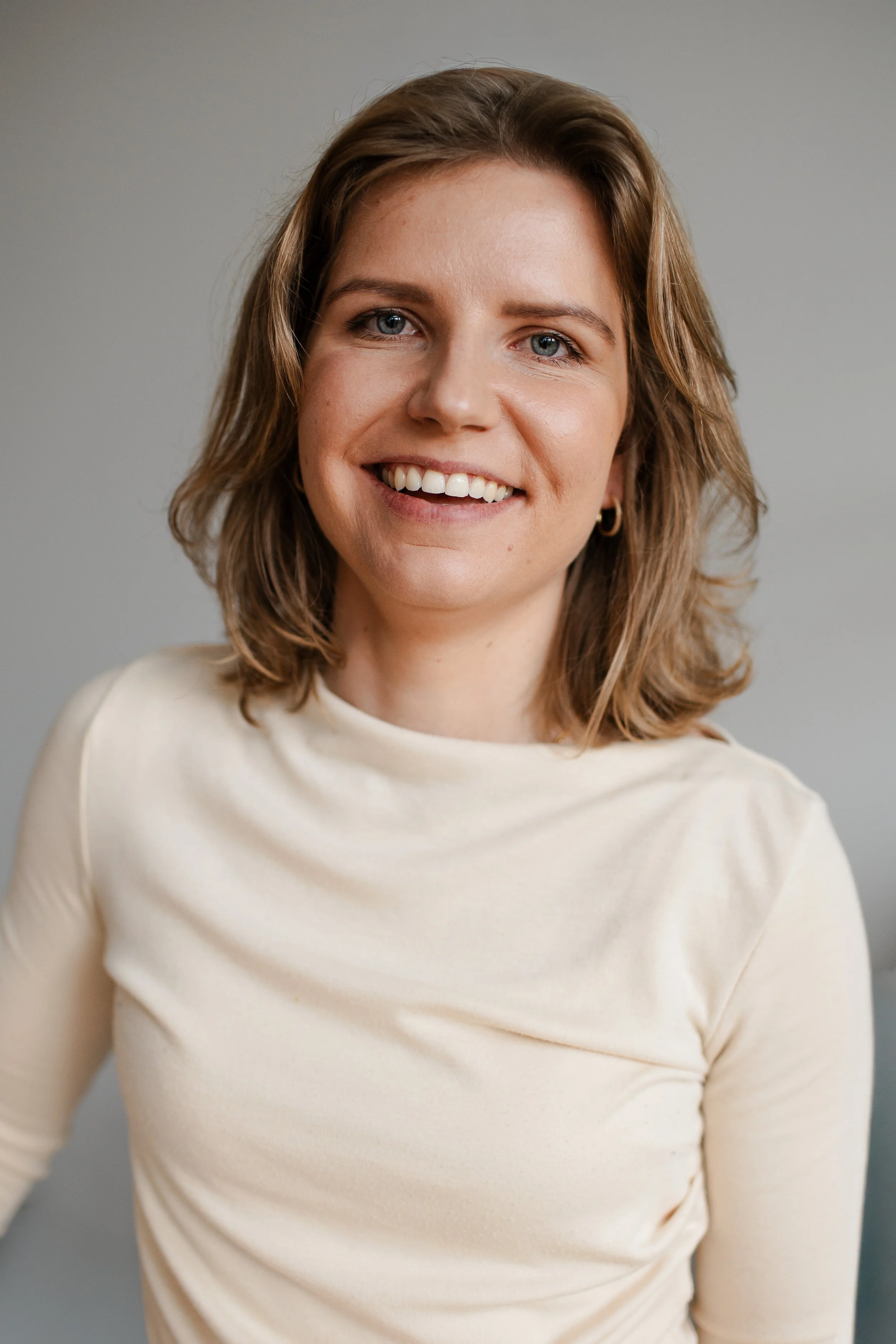 A woman with shoulder-length brown hair and blue eyes smiling, wearing a cream-colored top.