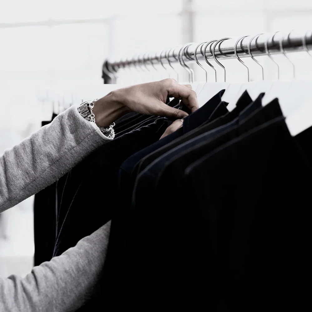 Een persoon die kleding op een kapstok hangt, met de focus op de hand en de kleding.