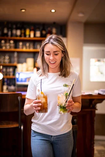 Een lachende vrouw houdt twee cocktails in een bar.