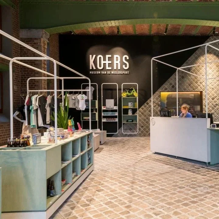 Interieur van het Koers WIELERSPORT Museum, met merchandise, een balie en een medewerker achter de balie.