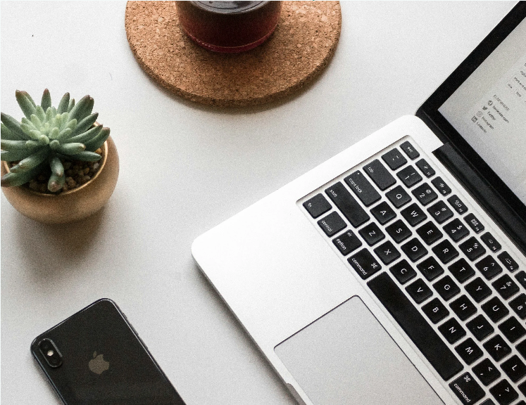 Vue partielle d'un bureau avec une plante succulente, un verre de boisson sur un sous-verre en liège, un smartphone, et un ordinateur portable.