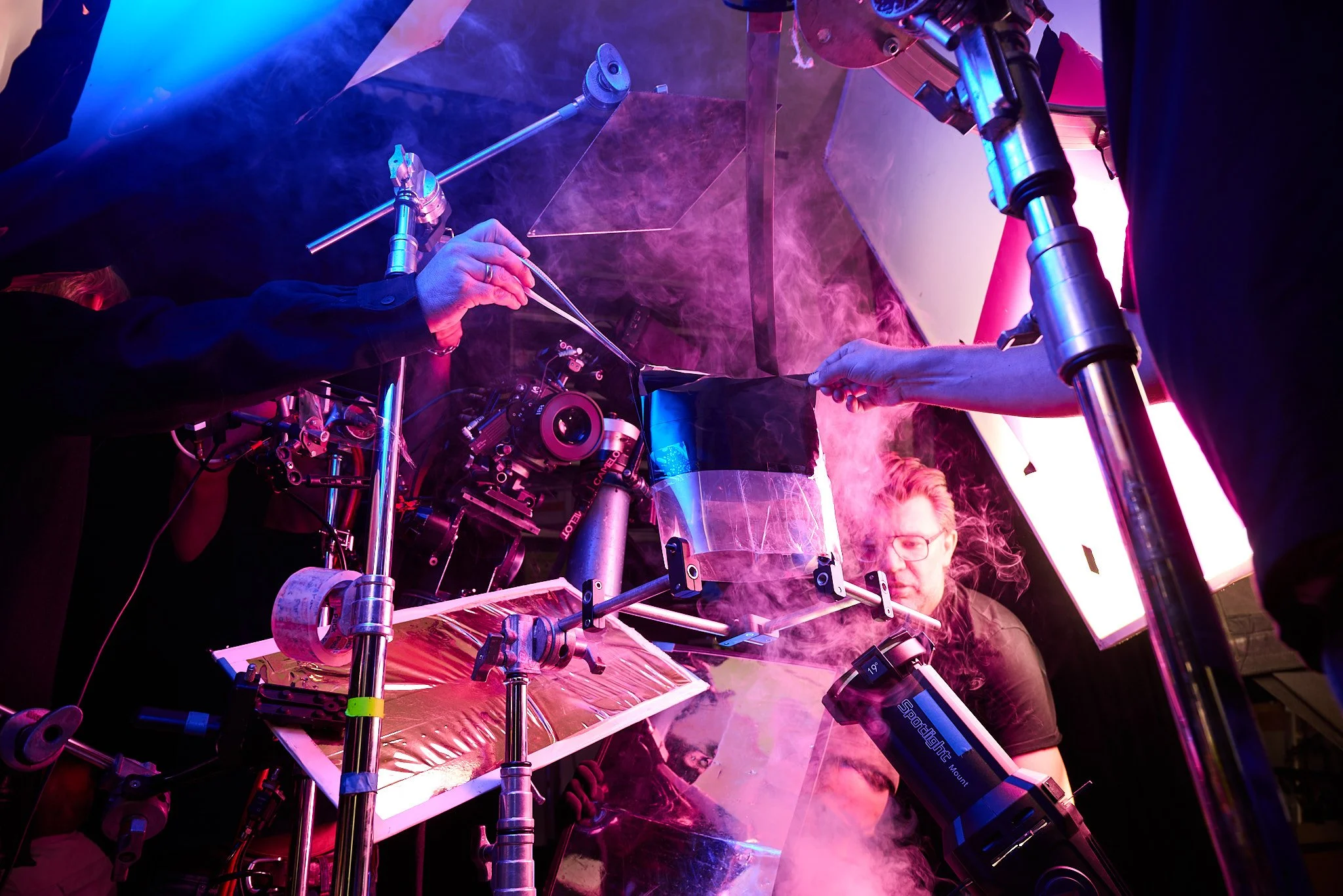 Scientists working with a telescope and complex equipment, with purple and pink lighting and fog.