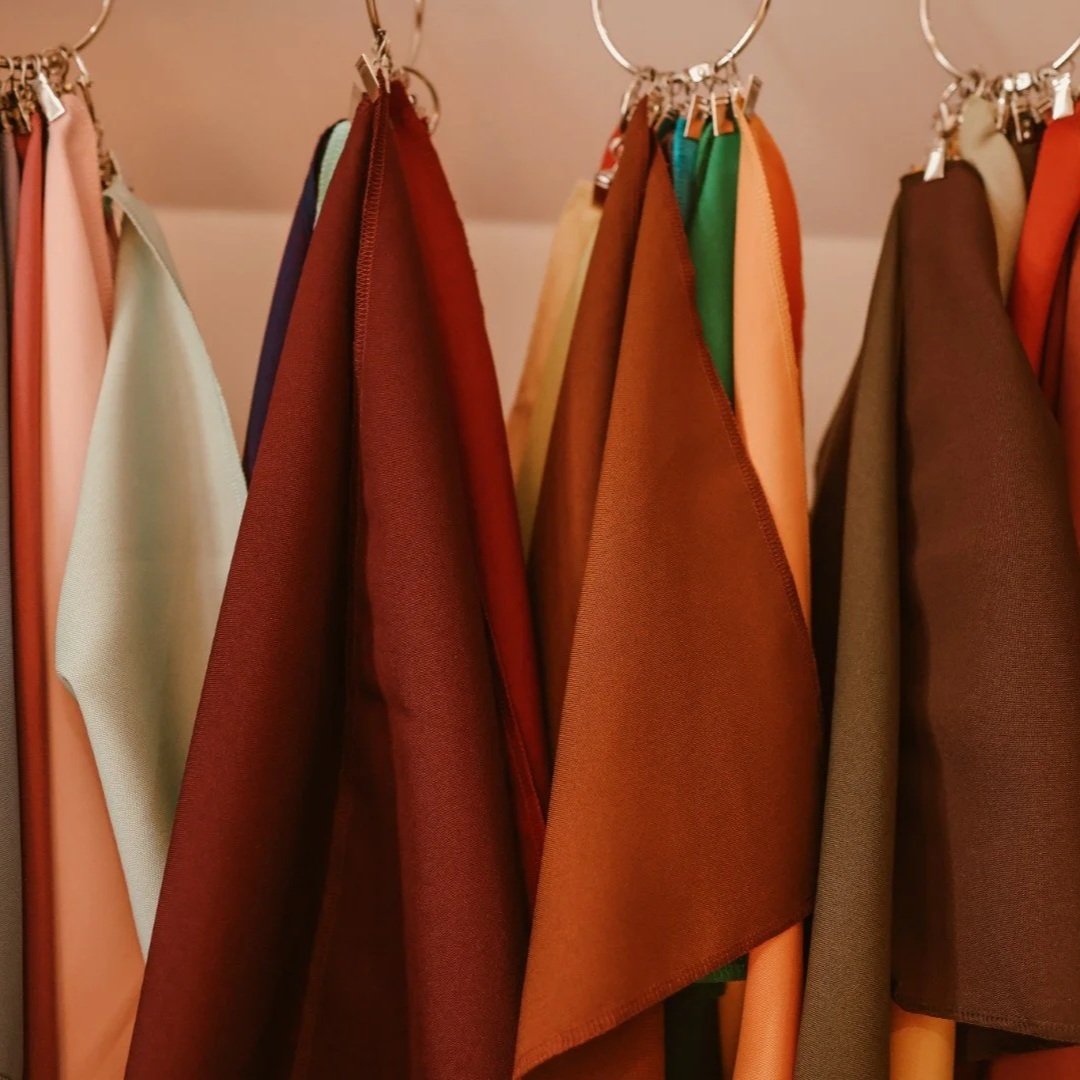 Een assortiment stoffen in verschillende kleuren, opgehangen aan metalen haken.