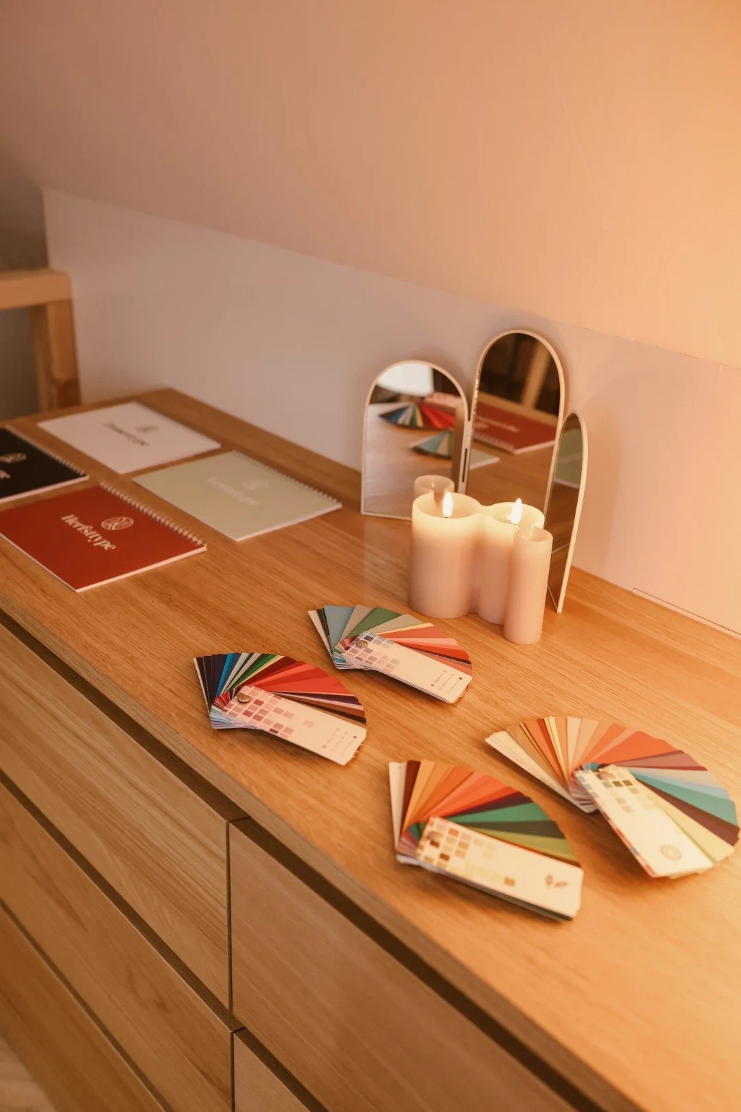Ladekast met kleurstalen, brochures en kleine spiegels, verlicht door kaarsen.