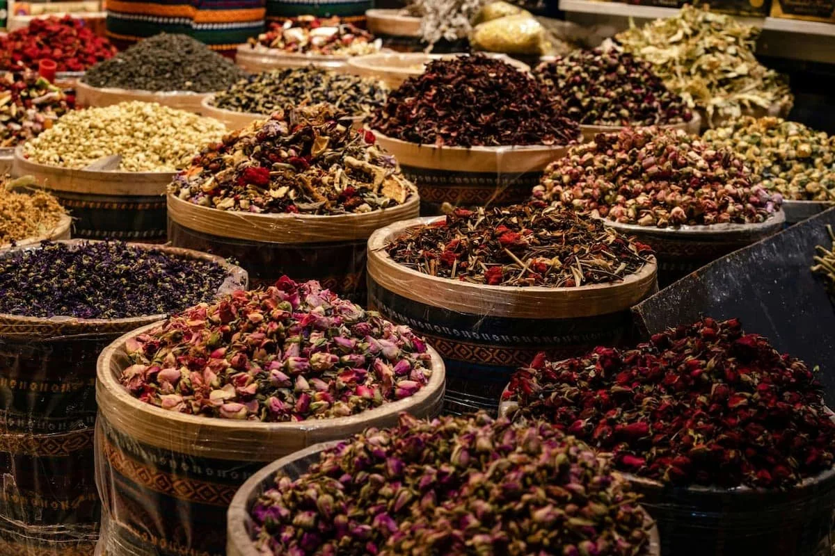 Various dried herbs, flowers, and spices in round baskets at a market.