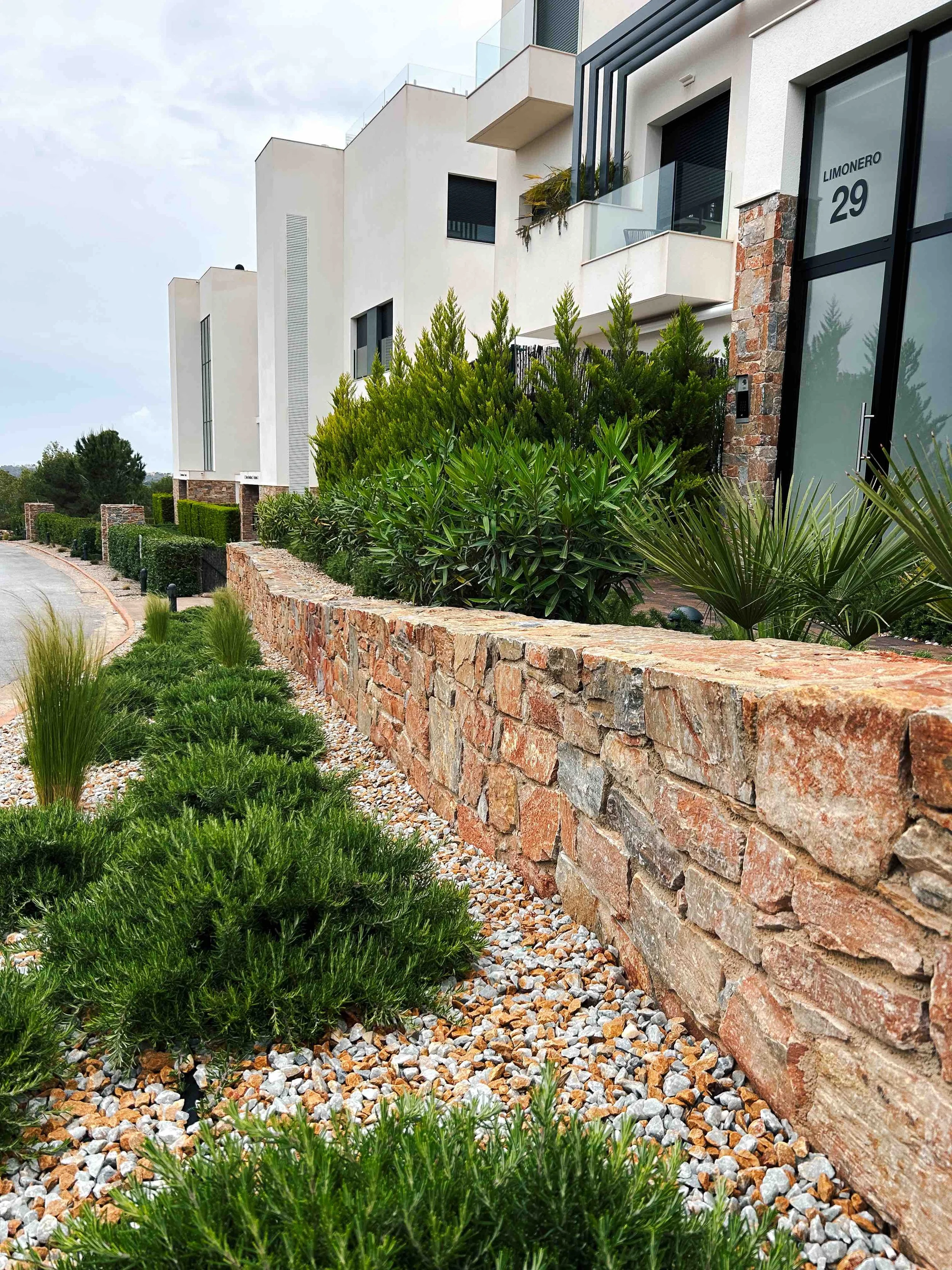 Vista de un moderno edificio residencial con línea de plantas y un muro de piedra decorativo en el jardín delantero.