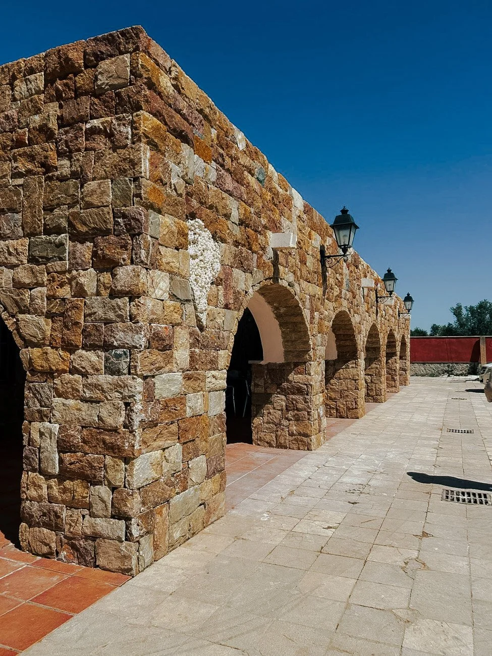 Estructura de muro de piedra con arcos y farolas en un día despejado y soleado.