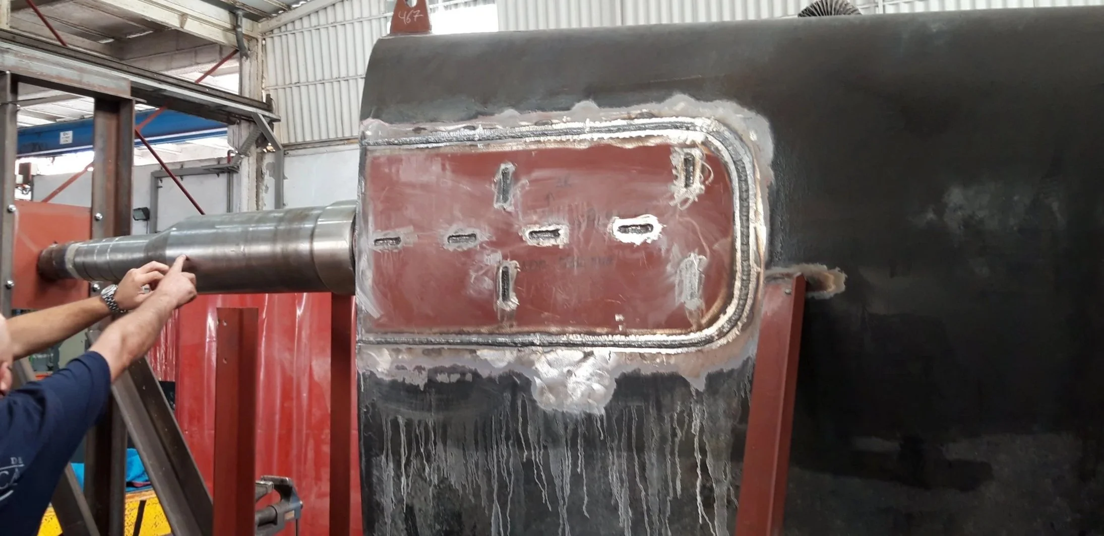 A person is inspecting a large industrial metal component on a machine in a factory setting.