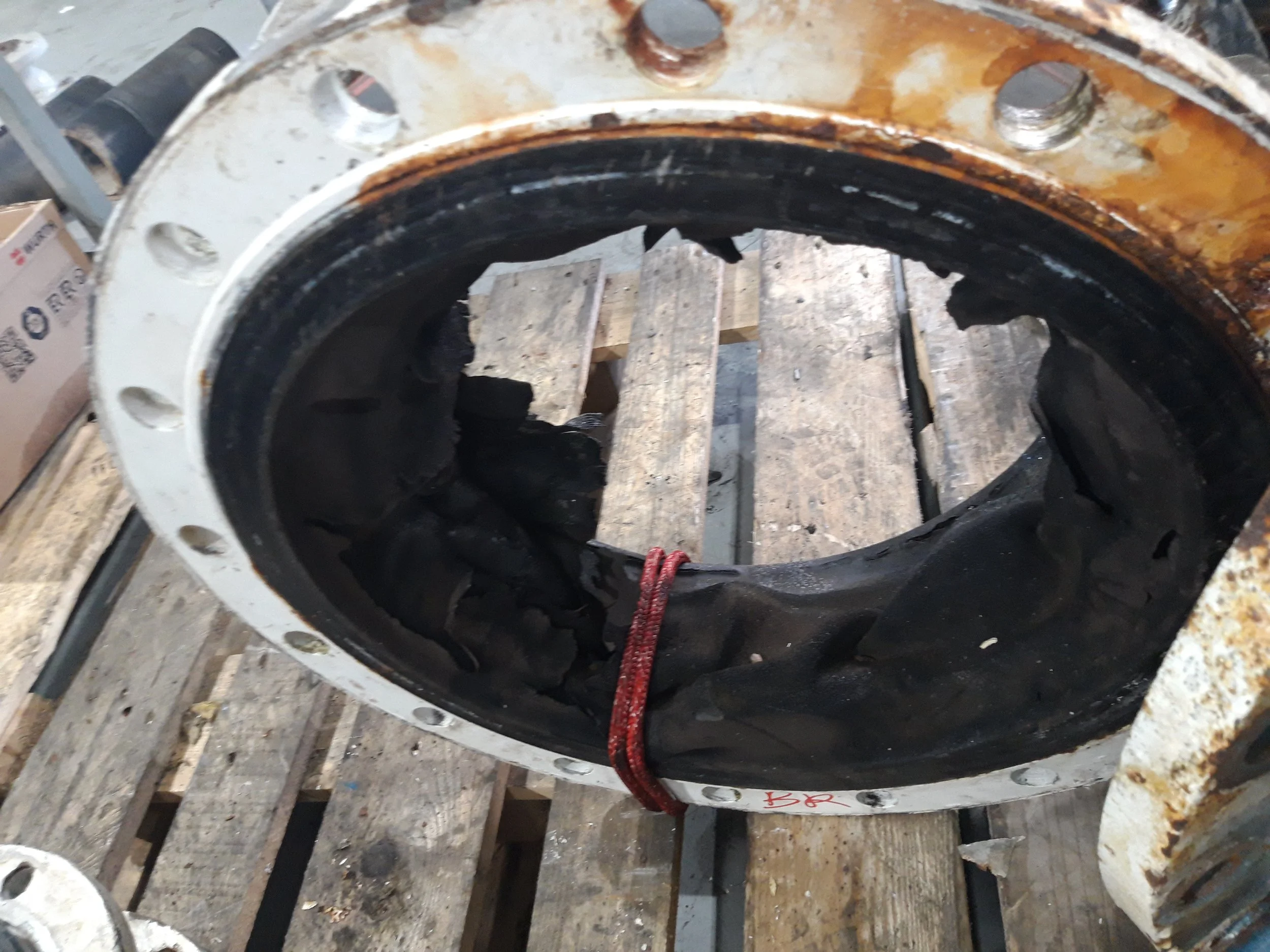 A large, rusted industrial bearing with a black rubber seal inside, placed on a wooden pallet.