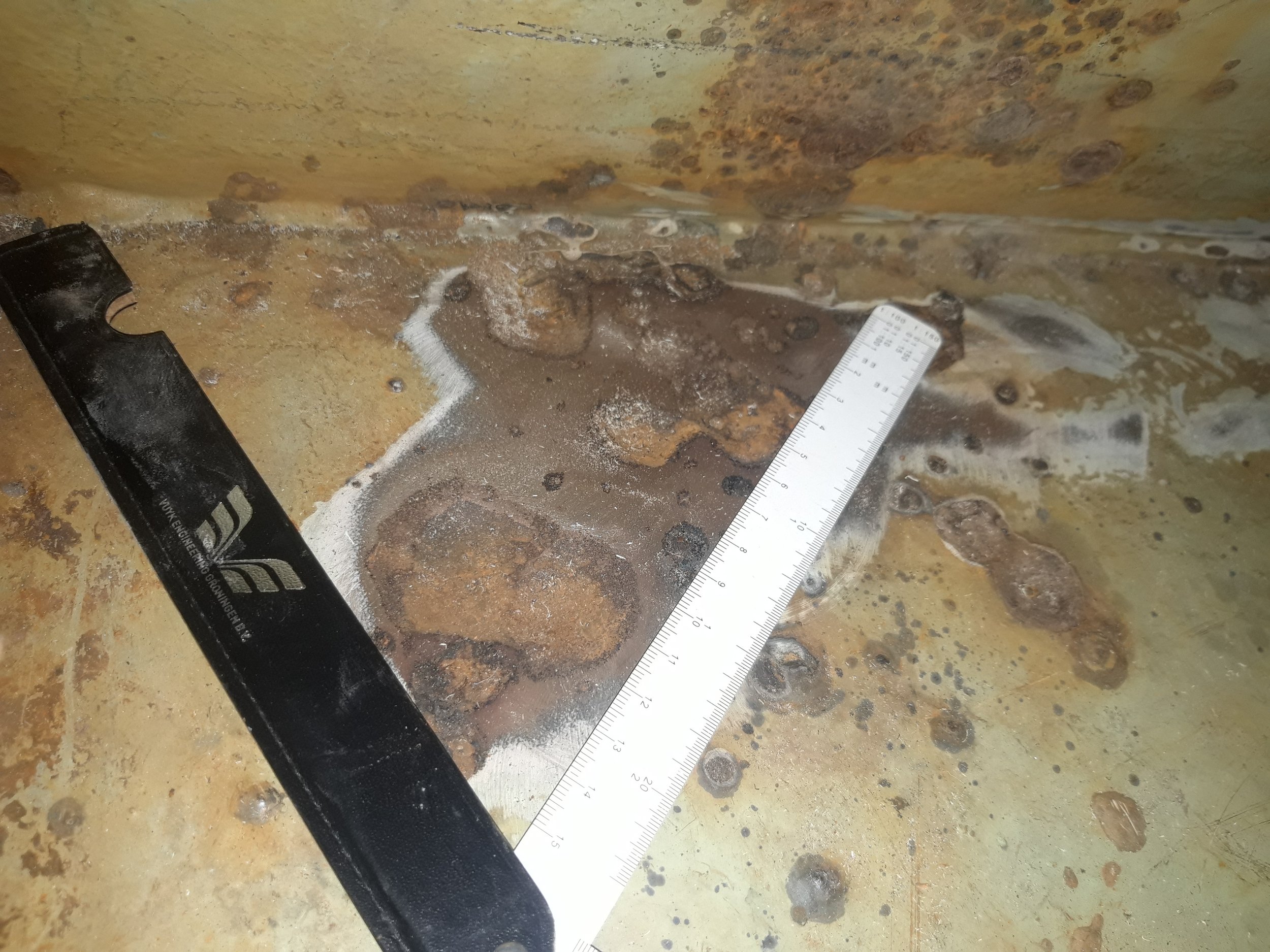 Rusty metal surface with a white ruler and a black tool.