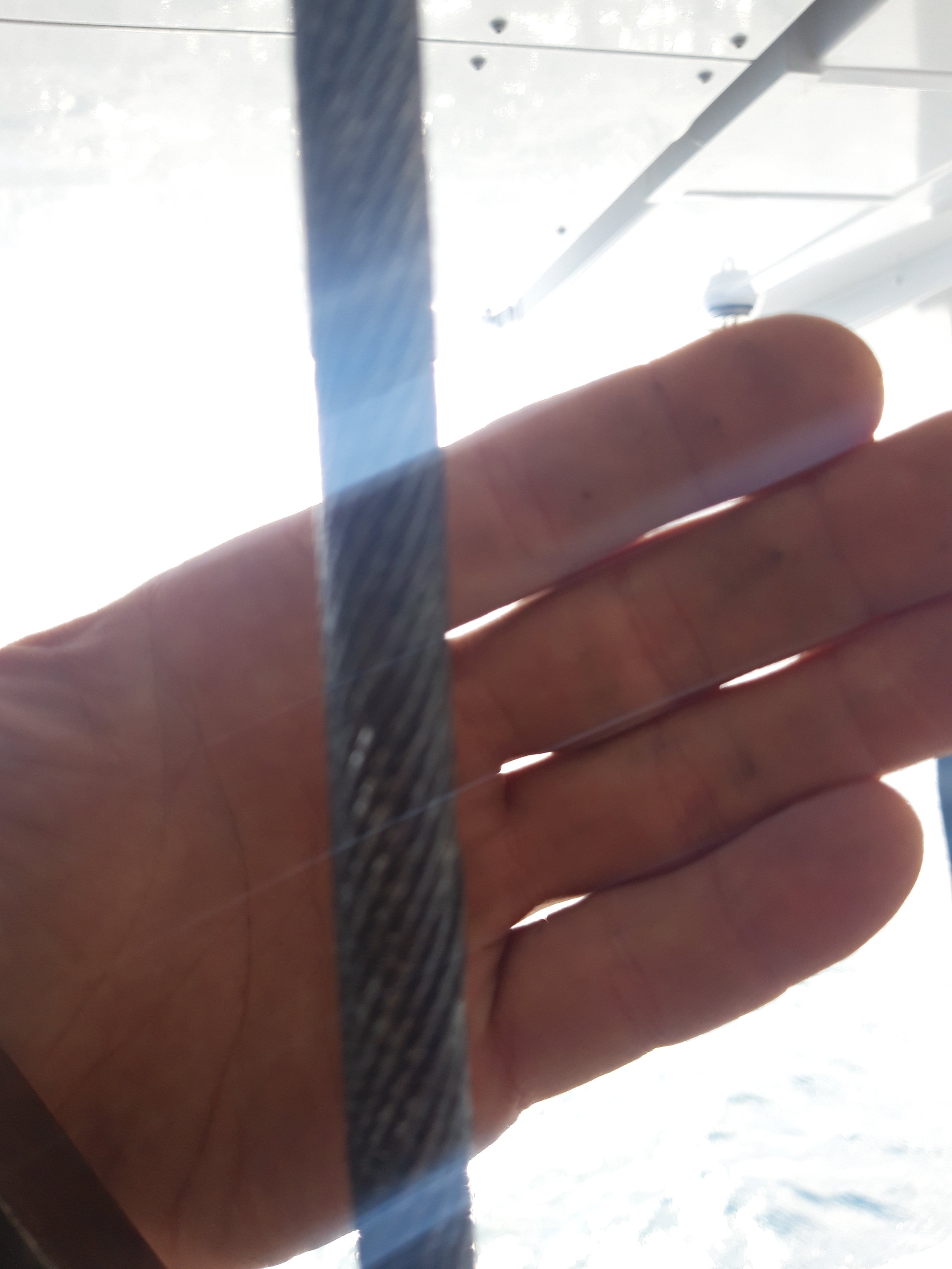Close-up of a hand with a black strap or cord in front of a bright background, possibly near water or outdoors.