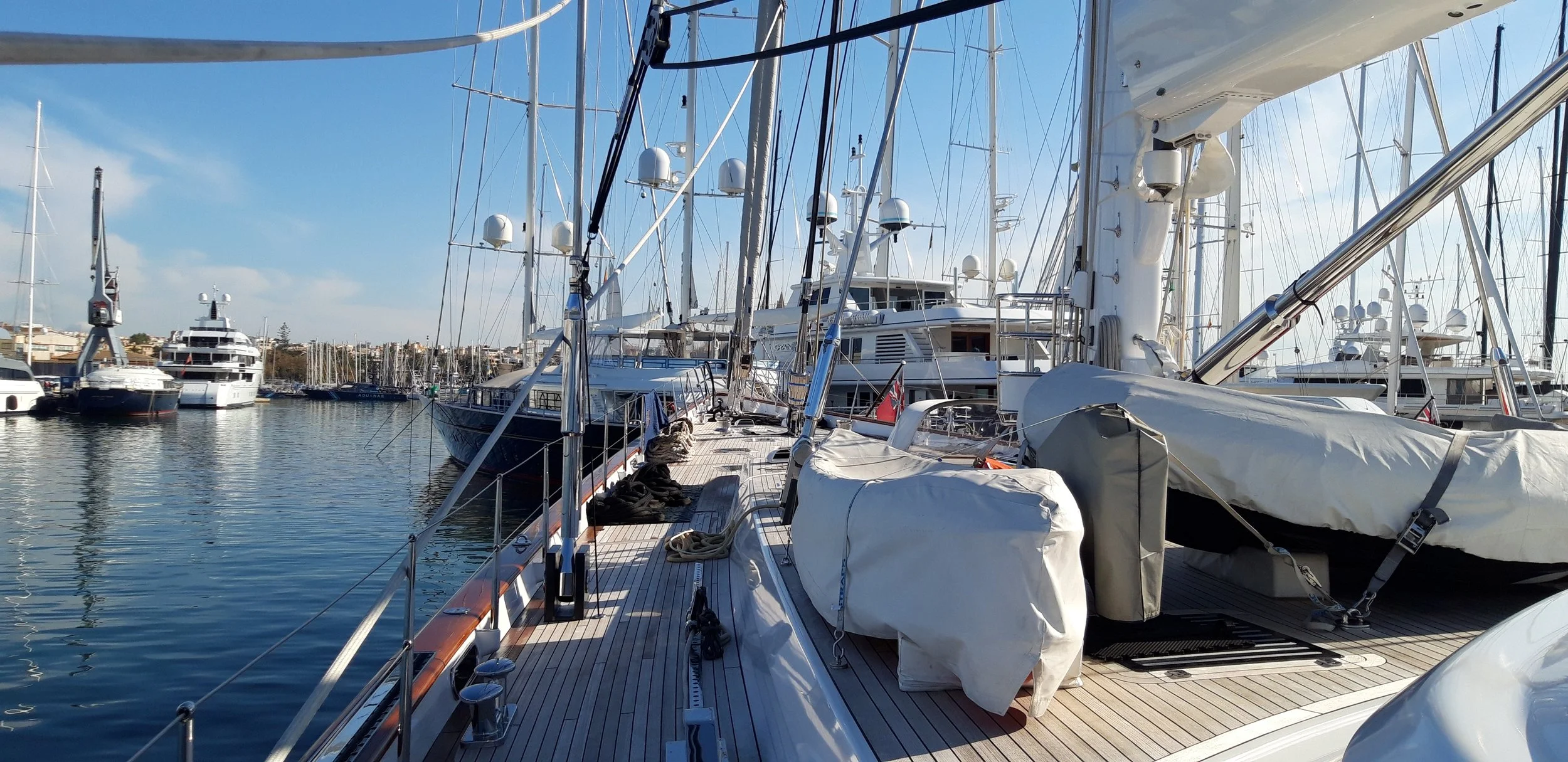 View of sailboats and yachts docked at a marina with clear blue sky and calm water.